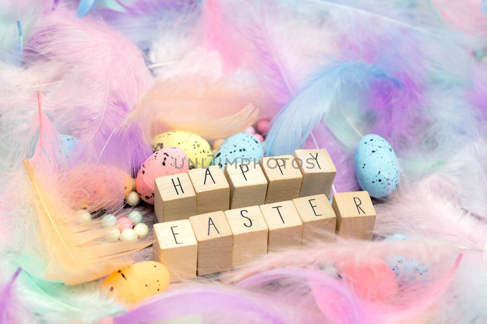 Happy Easter written with wooden cubes surrounded with beautiful pastel colored decorative feathers and eggs, April, Easter, Religion, Spring concept for background and greeting card top view bright colors
