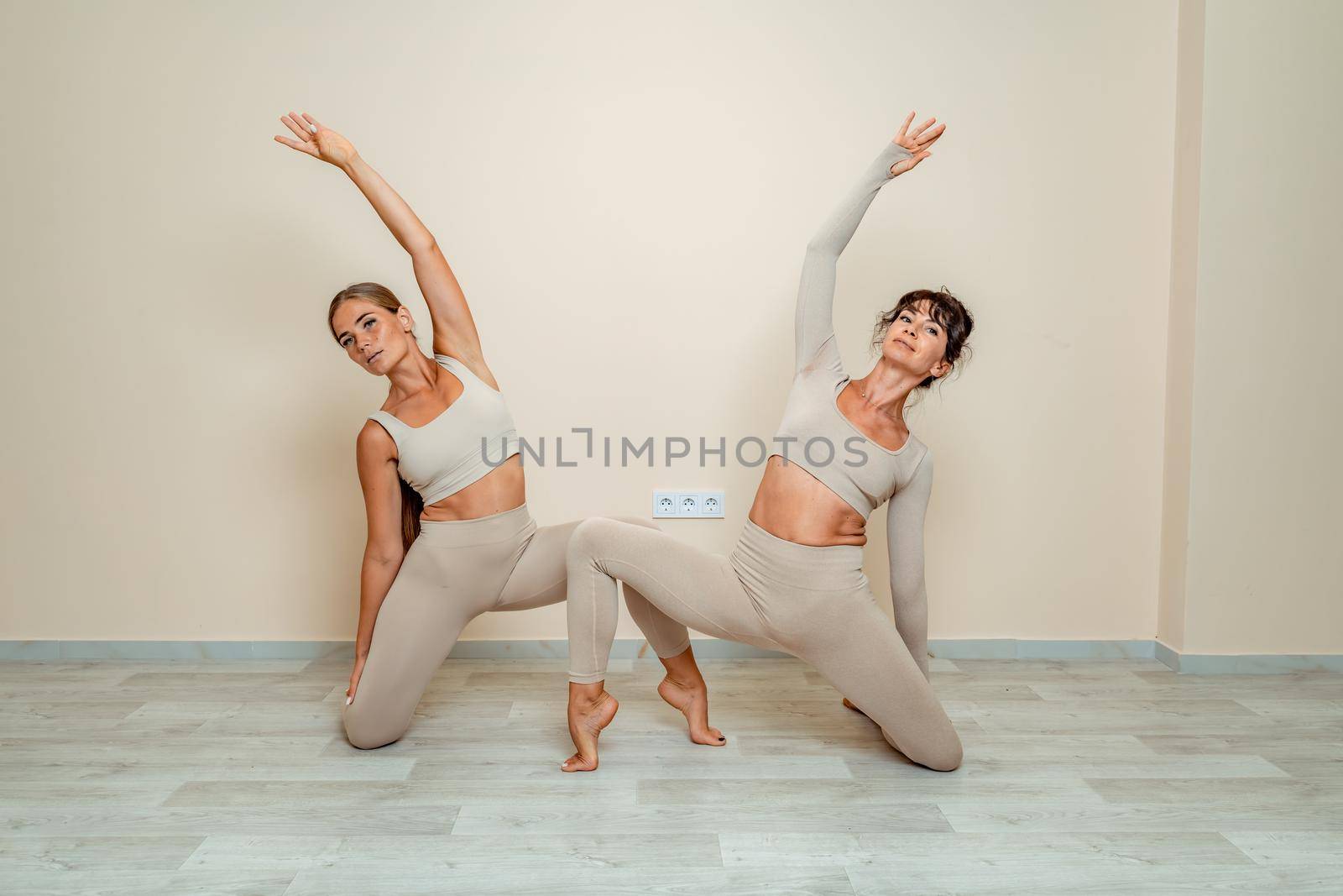 Fitness, pilates stretching exercises, a group of two attractive smiling mature women in beige sports clothes, train in a sports club. by Matiunina