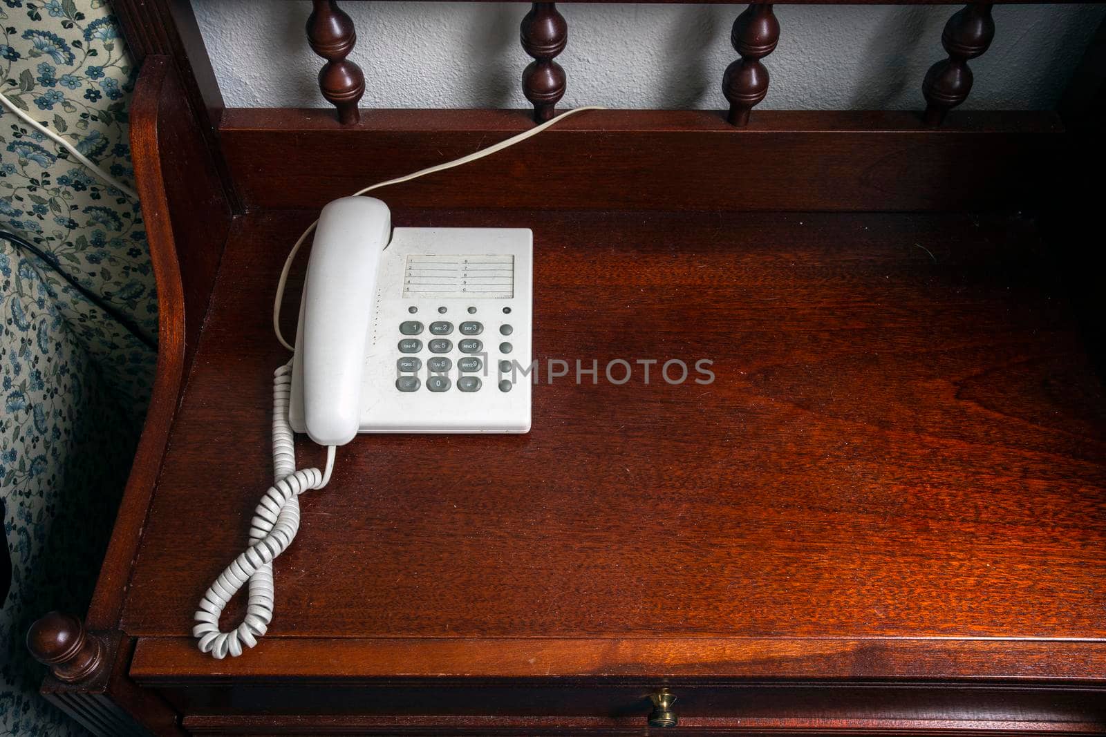 Old white telephone on vintage brown wooden nightstand near bed in bedroom antique design top vies with copy space by Annebel146