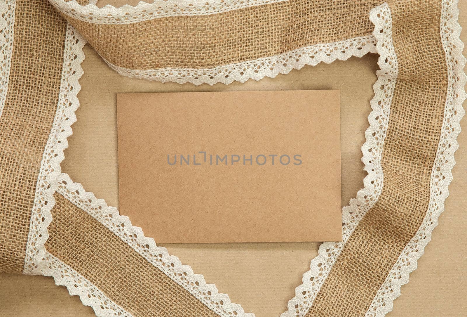 Flat Lay composition with blank brown plain greeting card surrounded with natural burlap ribbon on craft paper background texture, top view design, copy space natural colors space for text