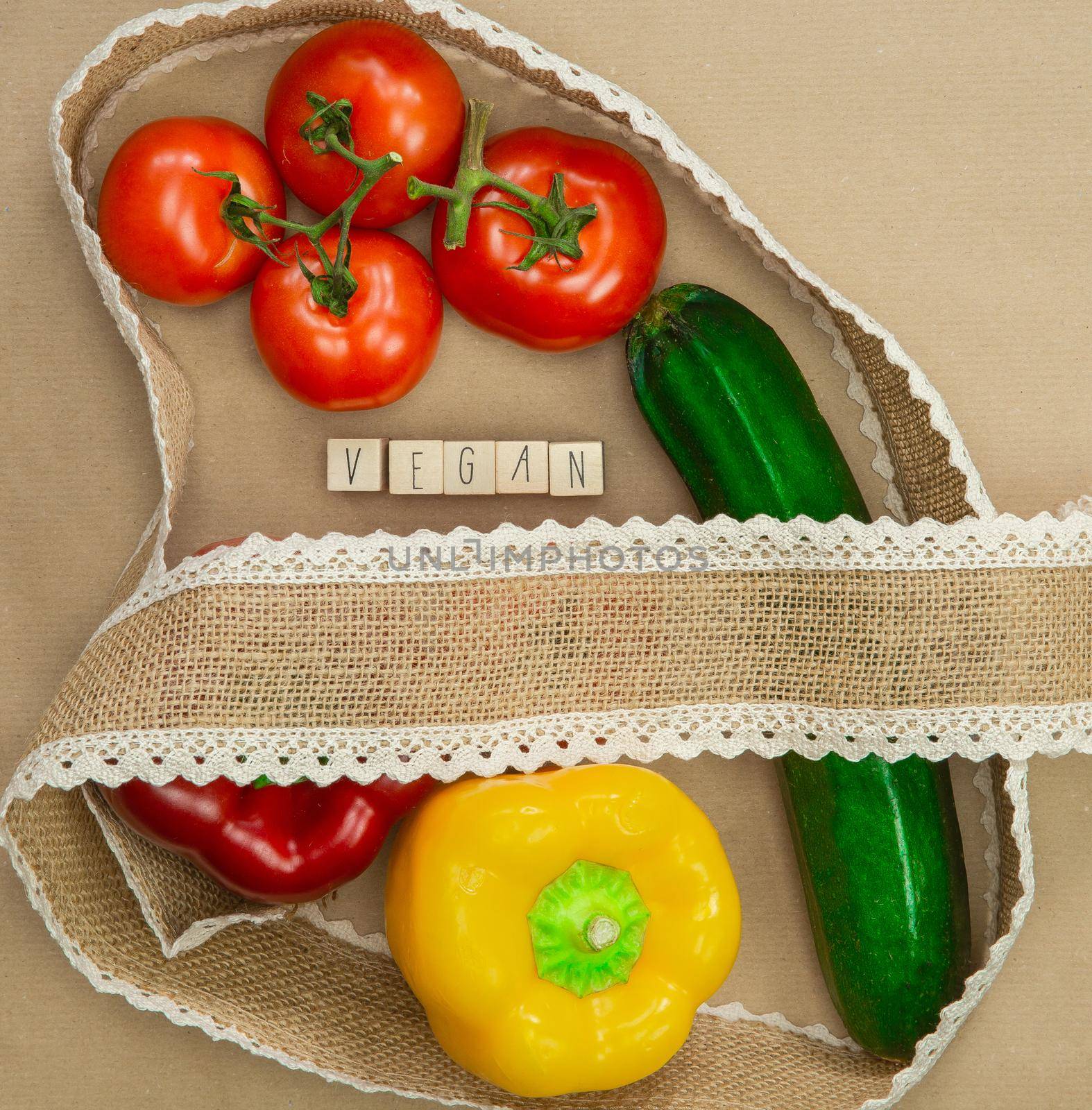 Vegan written with wooden cubes surrounded with fresh organic vegetables on brown craft paper with natural burlap ribbon top view, Vegan,Healthy food, Vegetarian concept background