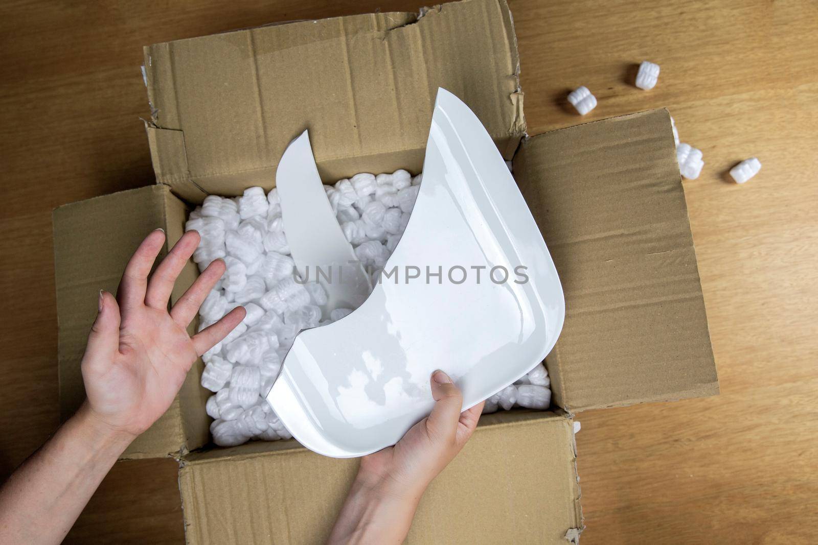 Broken plate in damaged cardboard box top view, damaged home delivery unpacking box close up