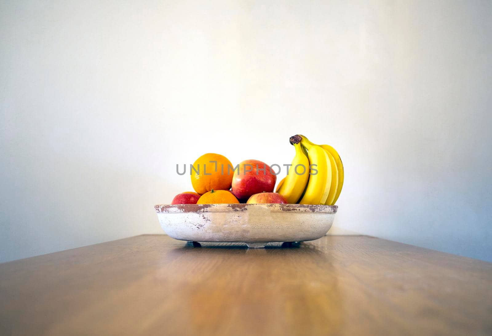 Healthy fresh fruit bowl on wooden table with Bananas, oranges and apples near white wall modern design on wooden table, copy space healthy still life front view home decoration