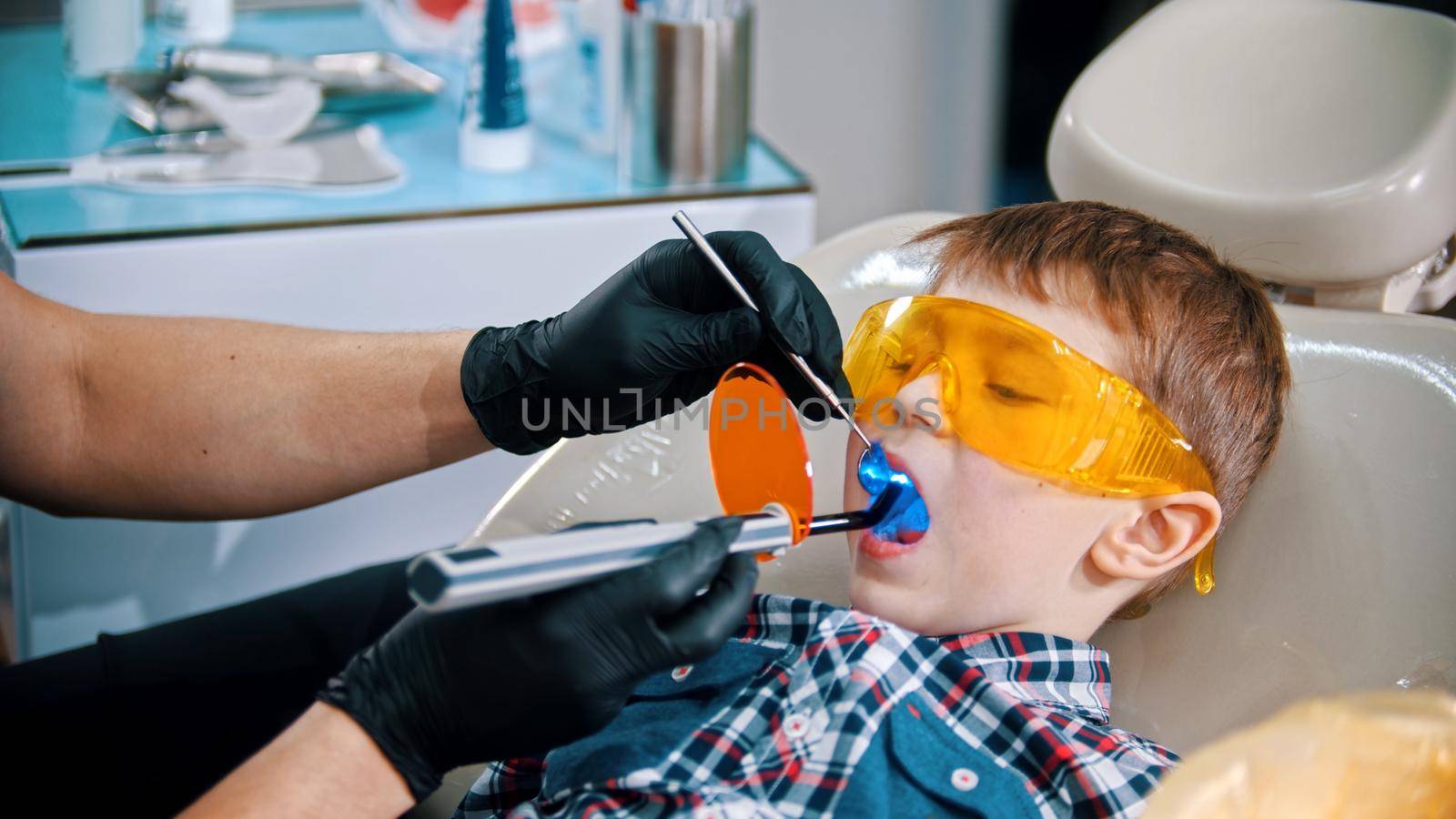 A little boy having his tooth done in the clinic - putting the photopolymer lamp with blue light in the mouth. Mid shot