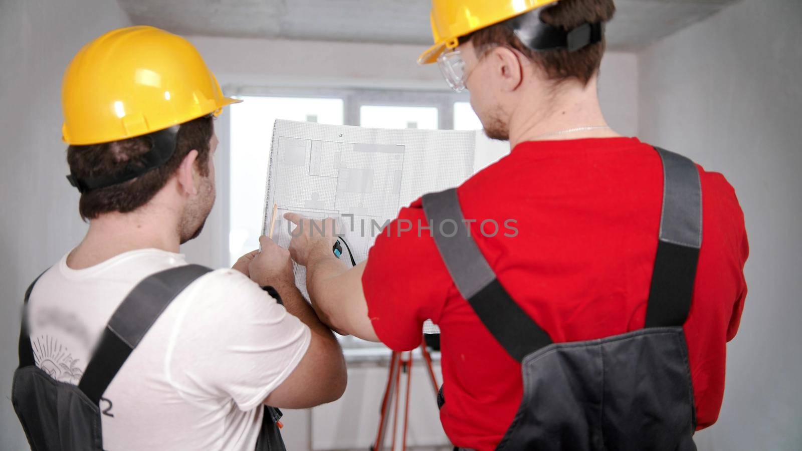 Two men workers looking at the layout of new apartment. Mid shot