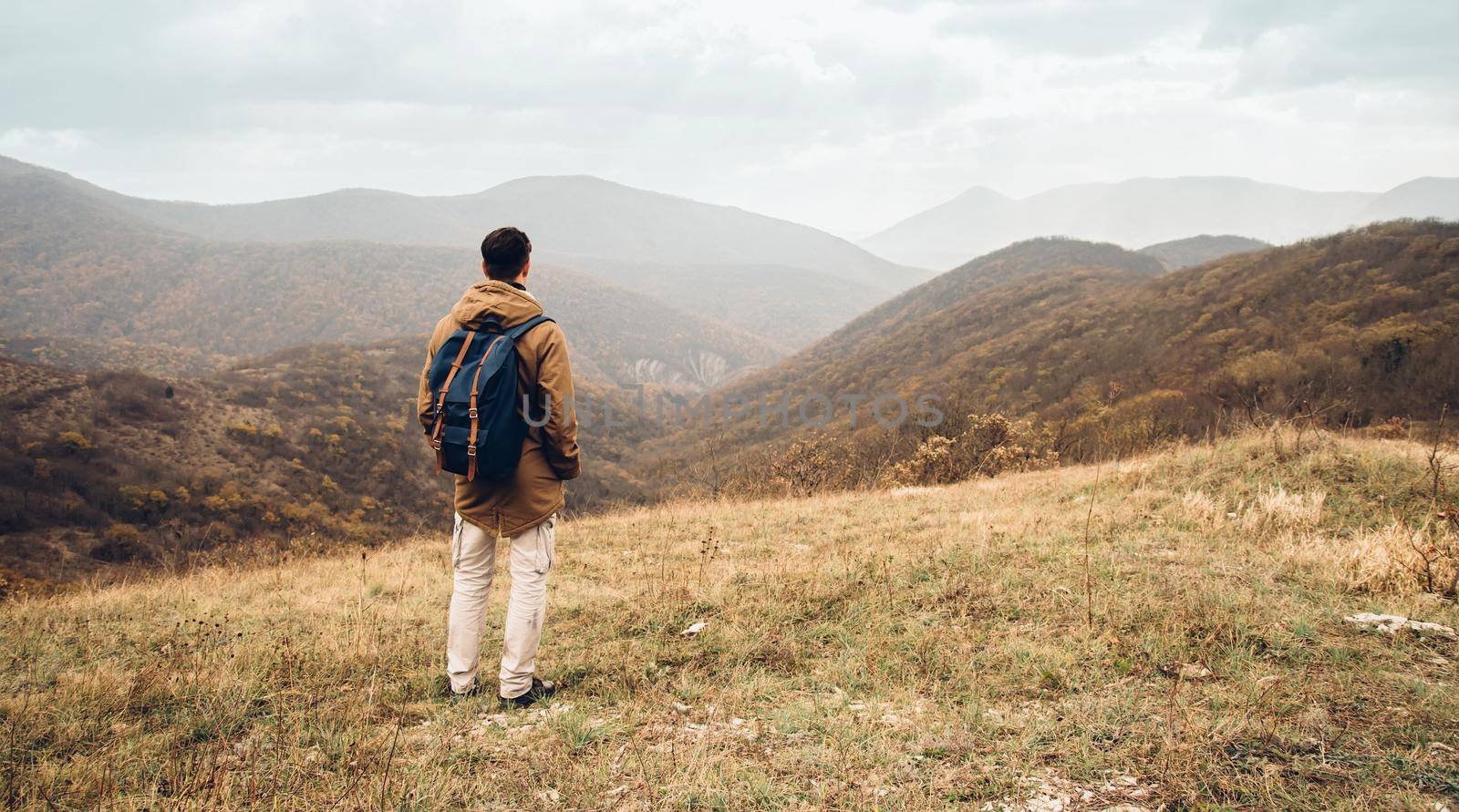Hiker man with backpack standing on hill and enjoying by scenic of mountains, rear view