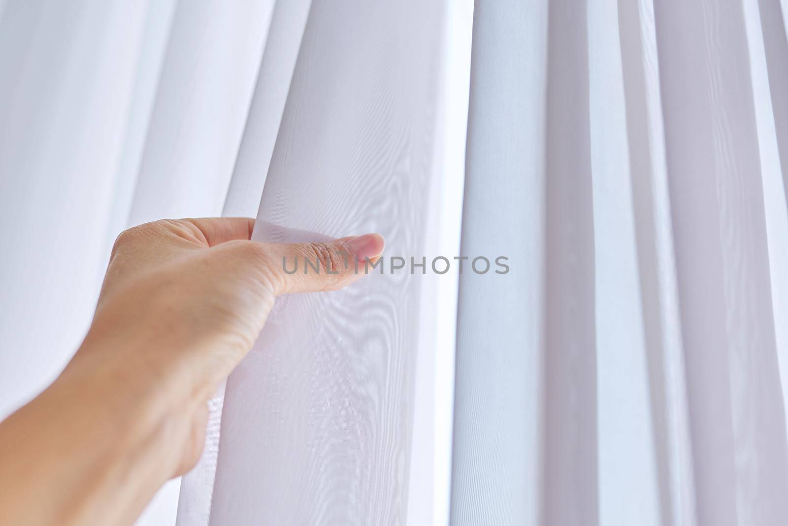 Close up of white tulle curtain on the window, woman hand touching fabric.