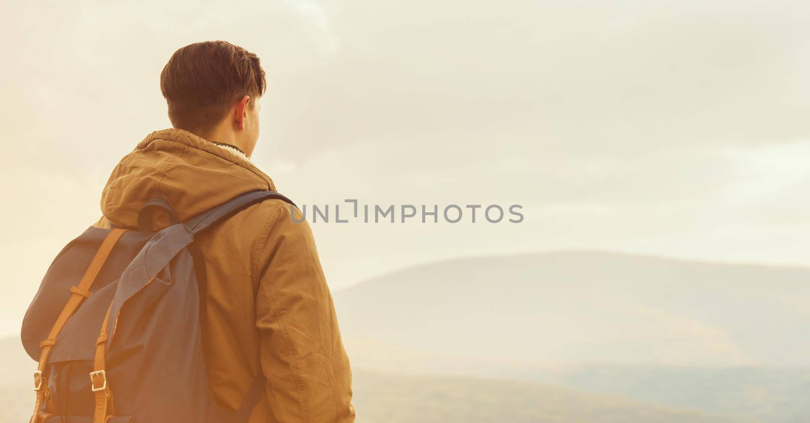 Hiker man with backpack enjoying landscape of mountains, rear view