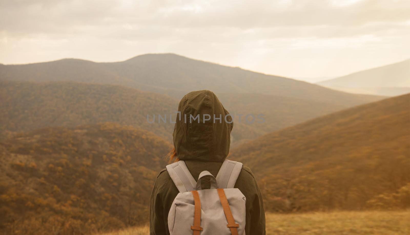 Hiker woman with backpack enjoying landscape of autumn mountains, rear view