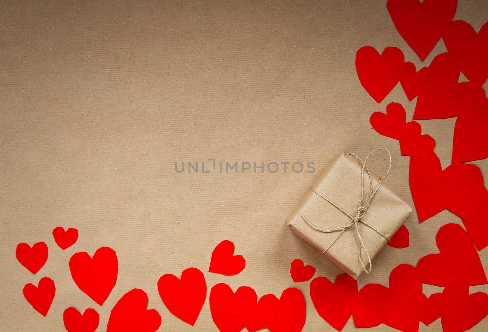 Gift box wrapped in kraft paper surrounded by red hearts on brown plain paper background, Valentines Day concept top view modern design, copy space romantic