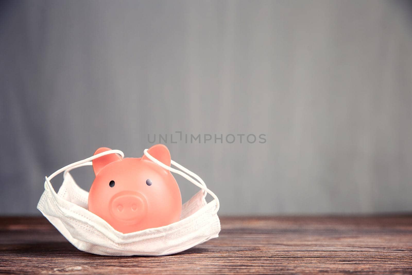 Inserting coin in piggy bank for savings with protective medical mask for pandemic, virus Covid-19, coronavirus,business,fianancial,saving concepy with copy space space for tect