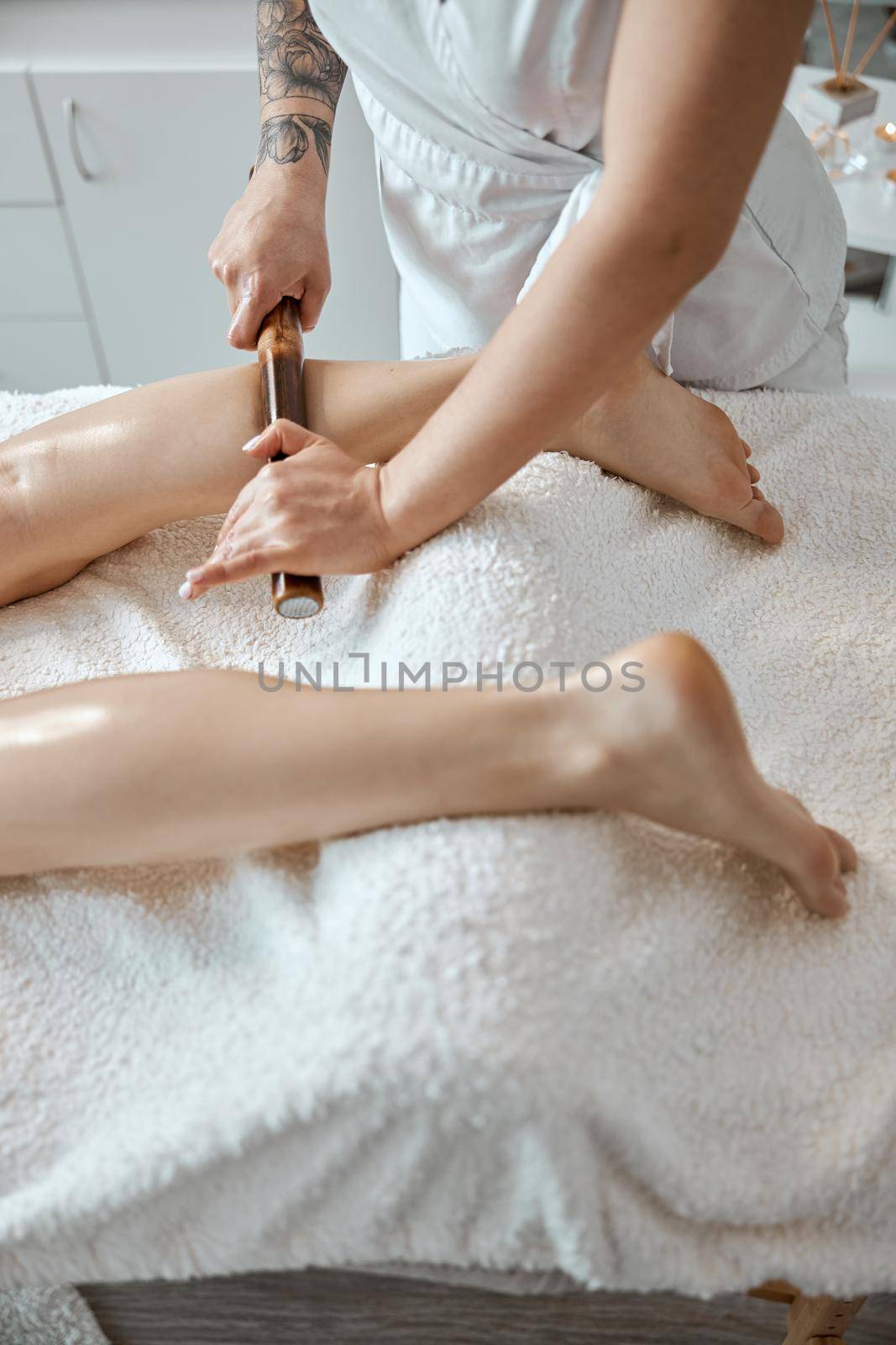 Conident female specialist is doing leg massage with bamboo stick to beautiful caucasean woman client