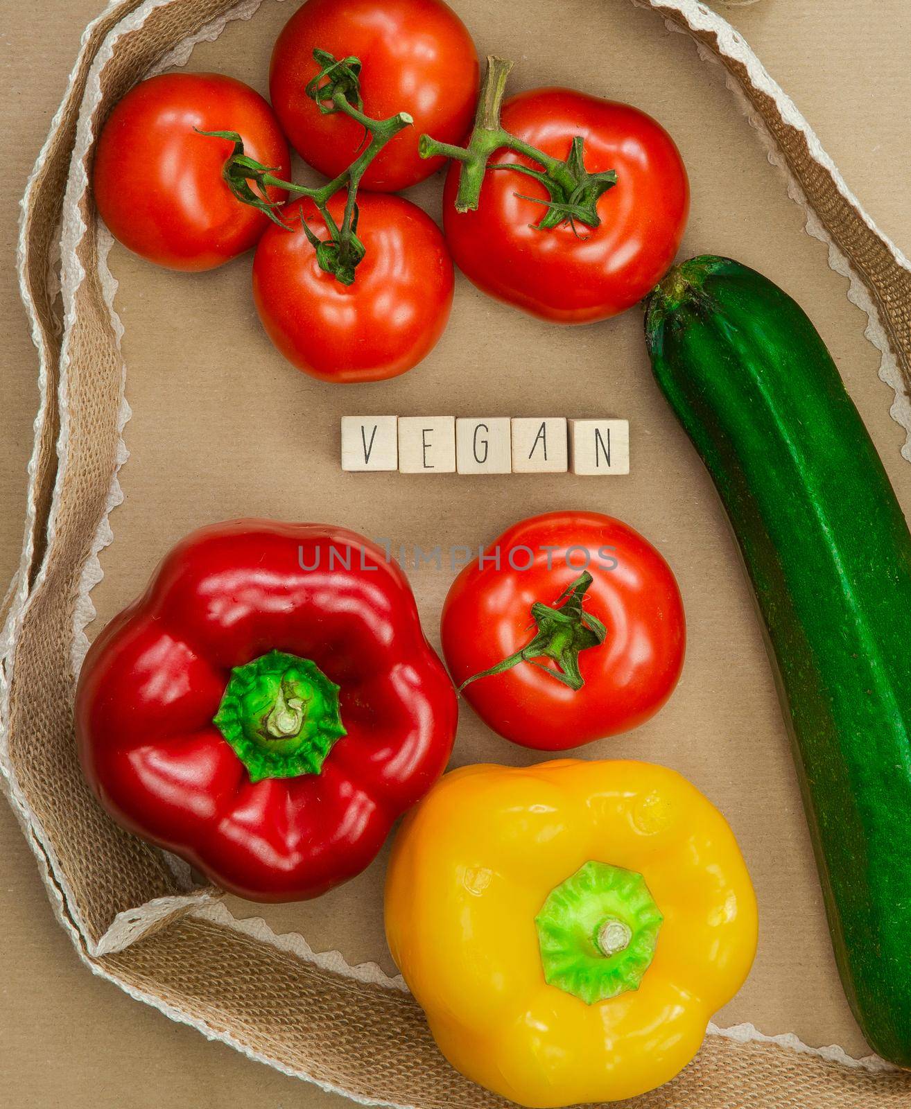 Vegan written with wooden cubes surrounded with fresh organic vegetables on brown craft paper with natural burlap ribbon top view, Vegan,Healthy food, Vegetarian concept background