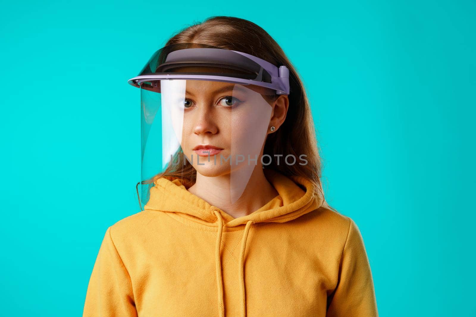 Young woman wearing medical protective face shield against blue background