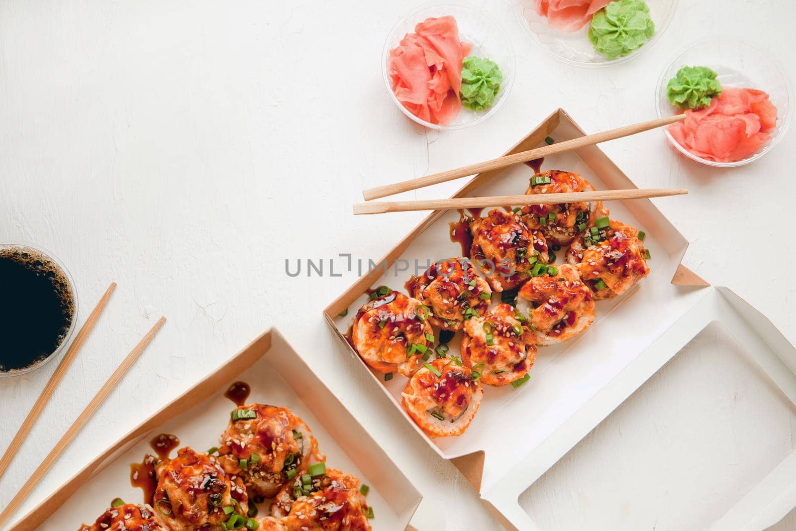 flat lay set with ginger and wasabi - baked sushi set with salmon in paper packaging on white background - bright delicious set of sushi rolls