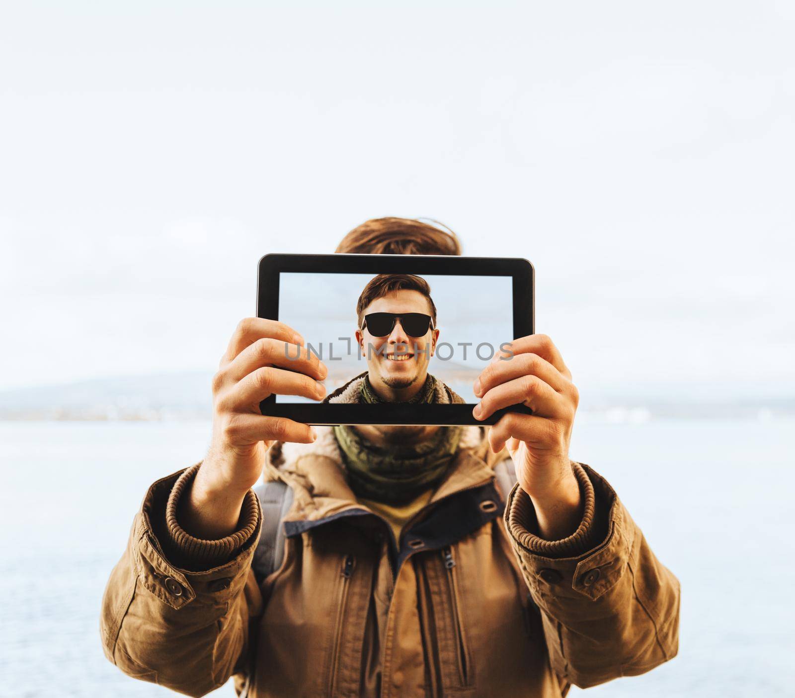 Hiker young man in sunglasses doing a self-portrait with him digital tablet on background of sea