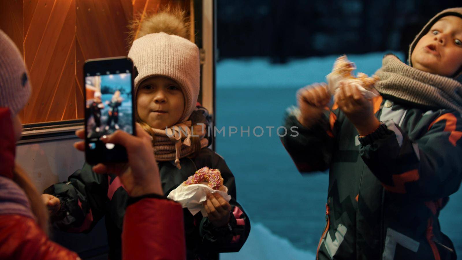 A woman mother taking photos of her children outdoors in winter. Mid shot