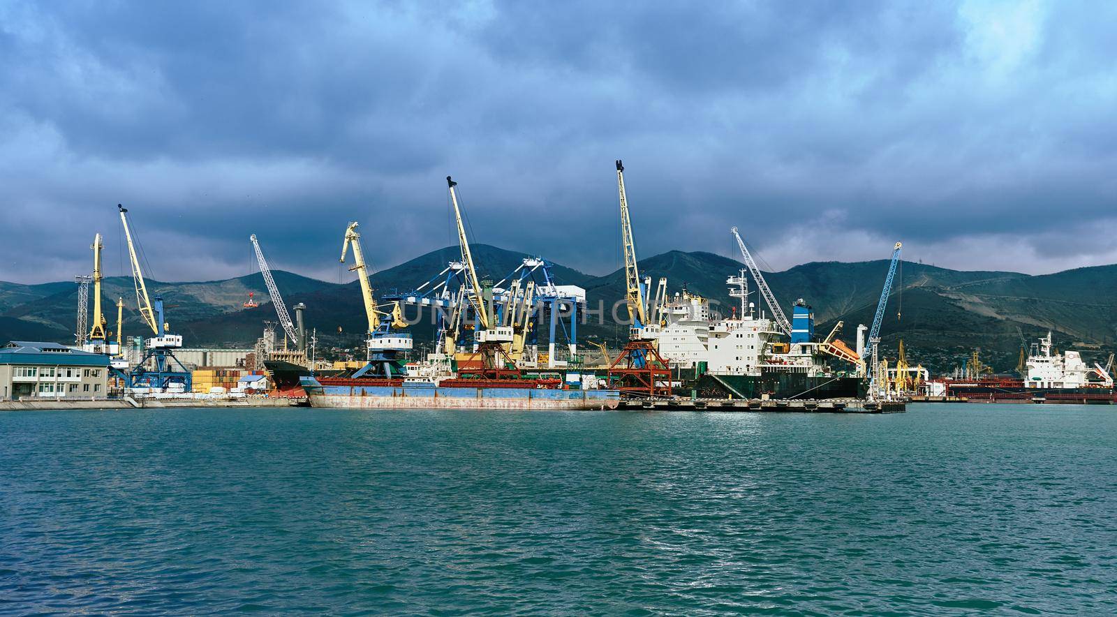 Seaport cargo crane in harbor on background of mountains and blue sky. Space for text in low part of image