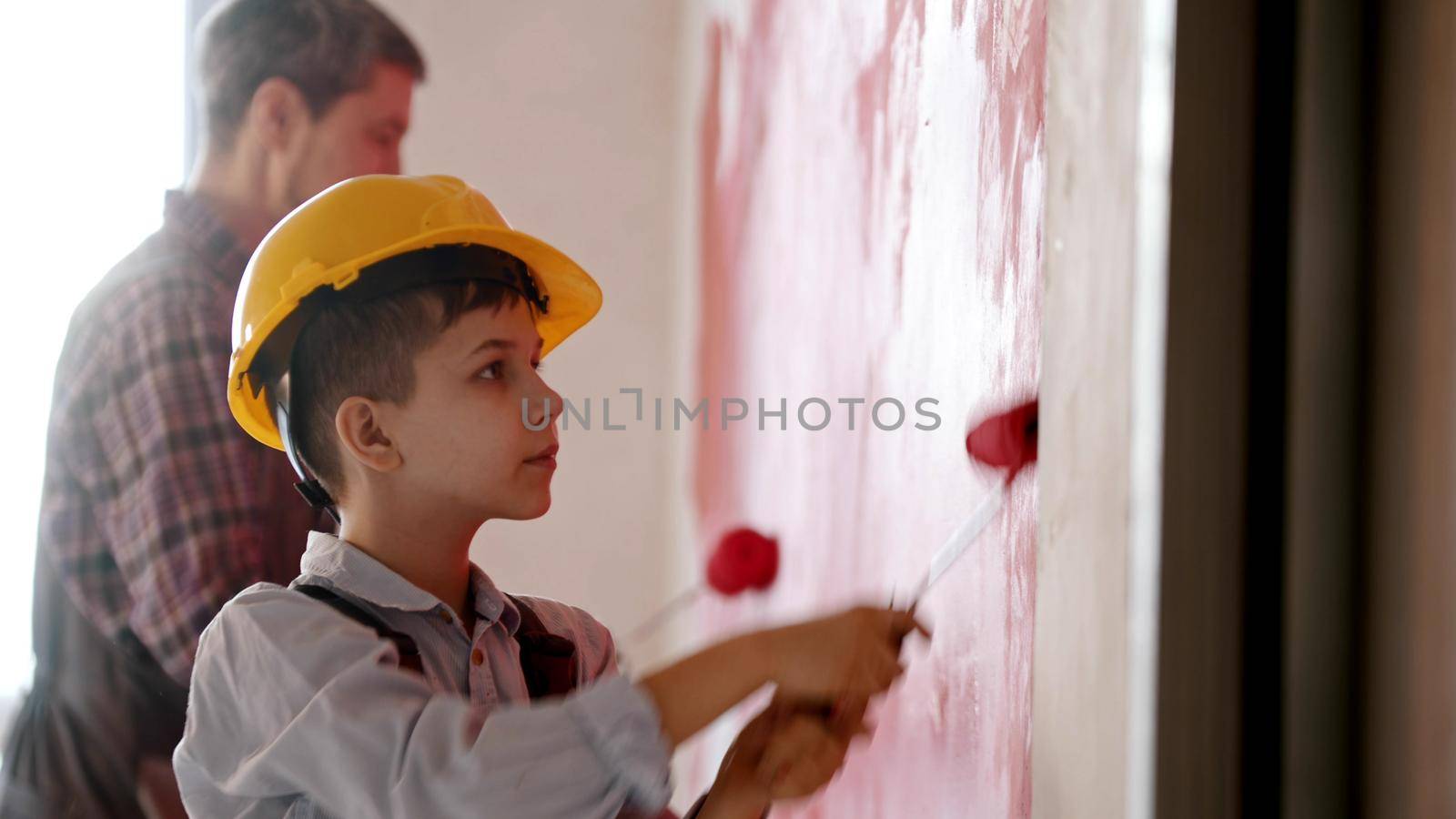 A little boy and his smiling father painting walls in red color. Mid shot