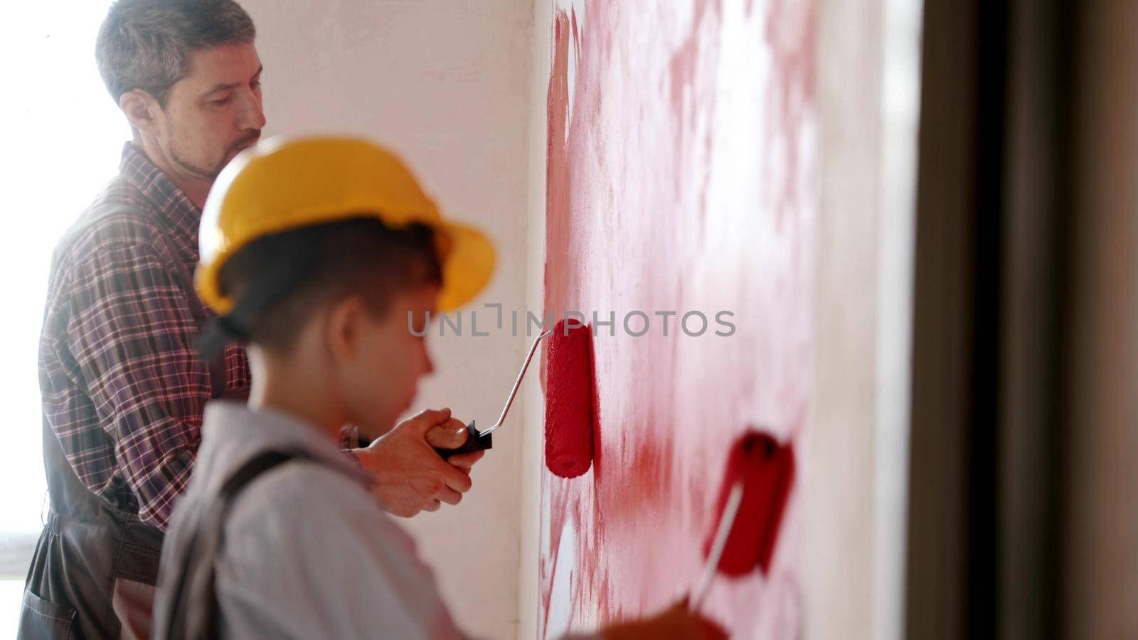 A little boy and his father painting walls in red color - a boy wearing helmet. Mid shot