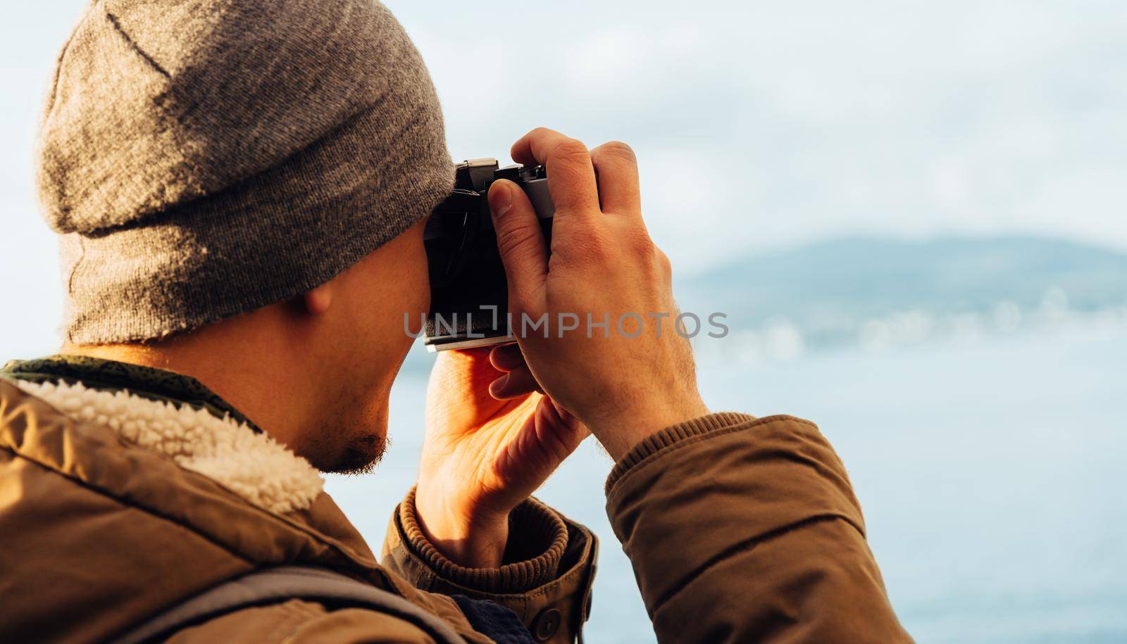 Traveler hipster guy takes photographs with vintage photo camera on coastline near the sea