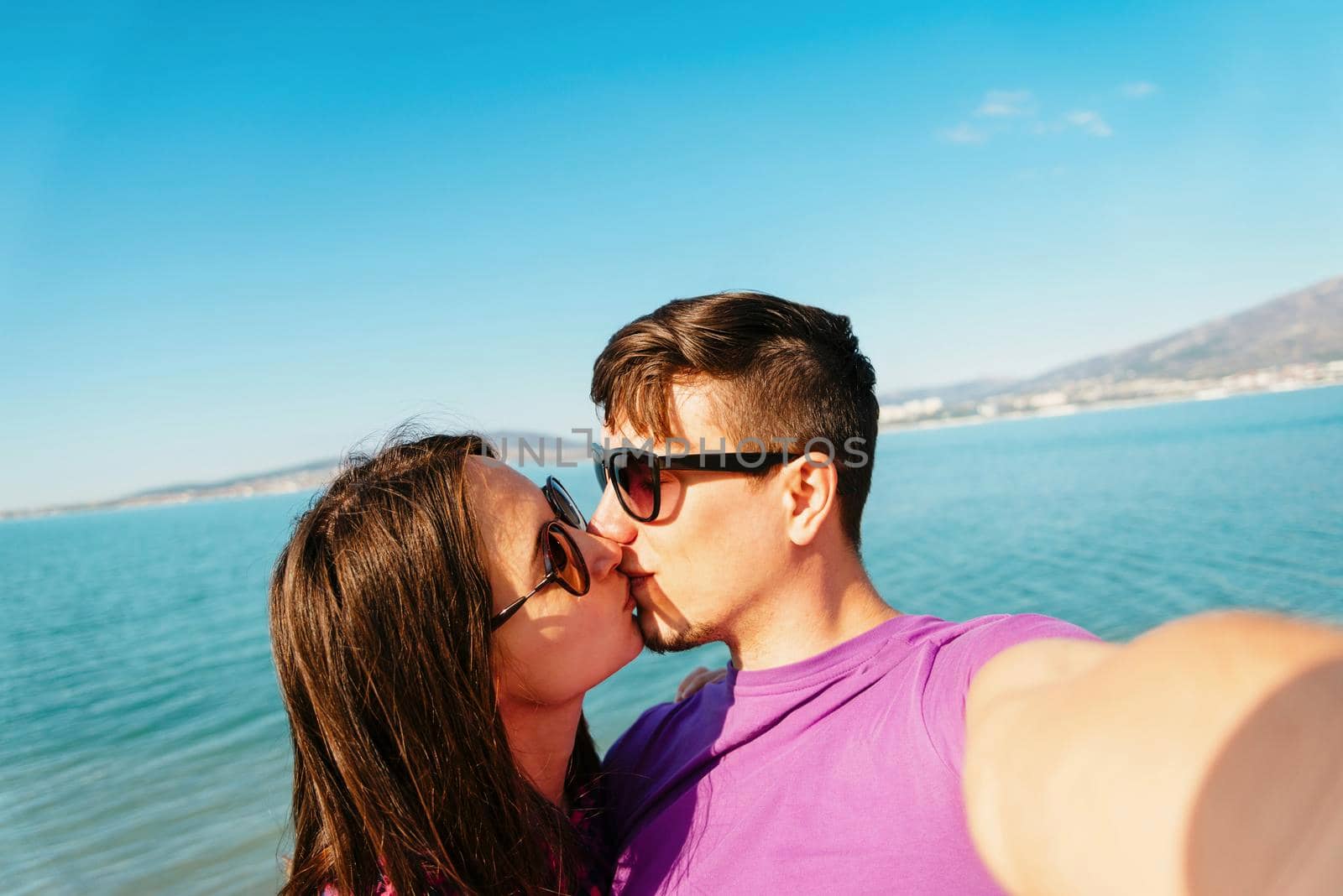 Happy young couple in love kissing and taking self-portrait on beach on background of blue sea