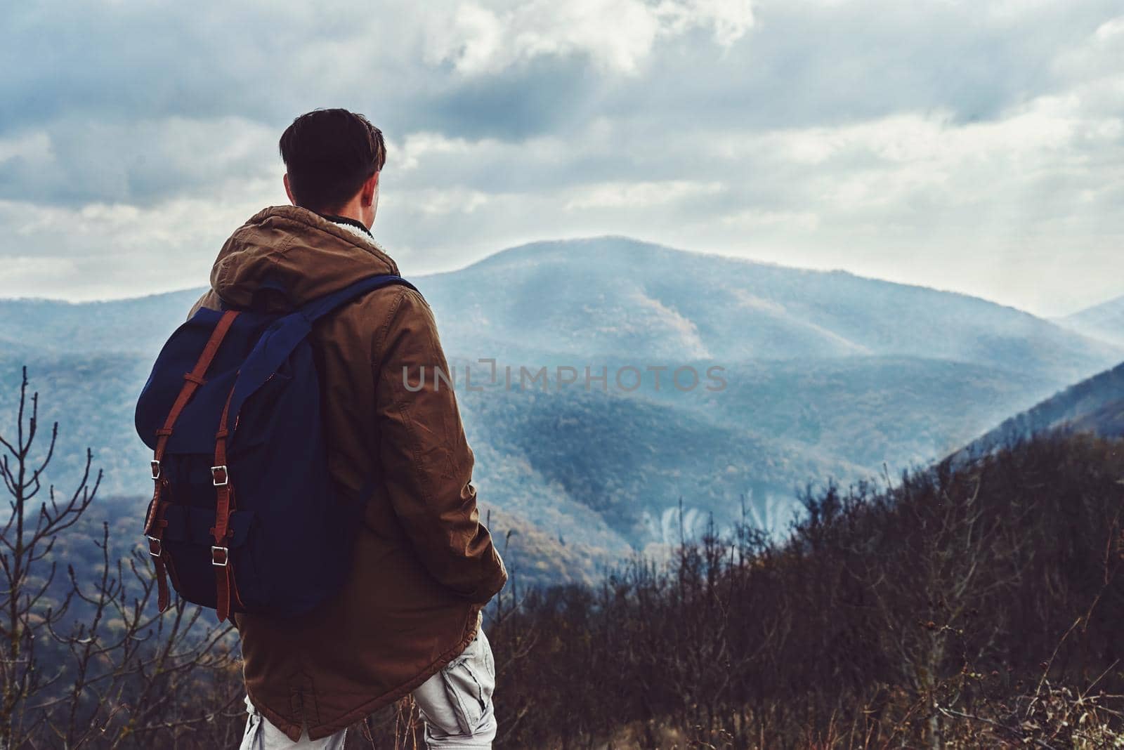 Hiker man with backpack looking at the mountains at autumn season, rear view. Low contrast effect