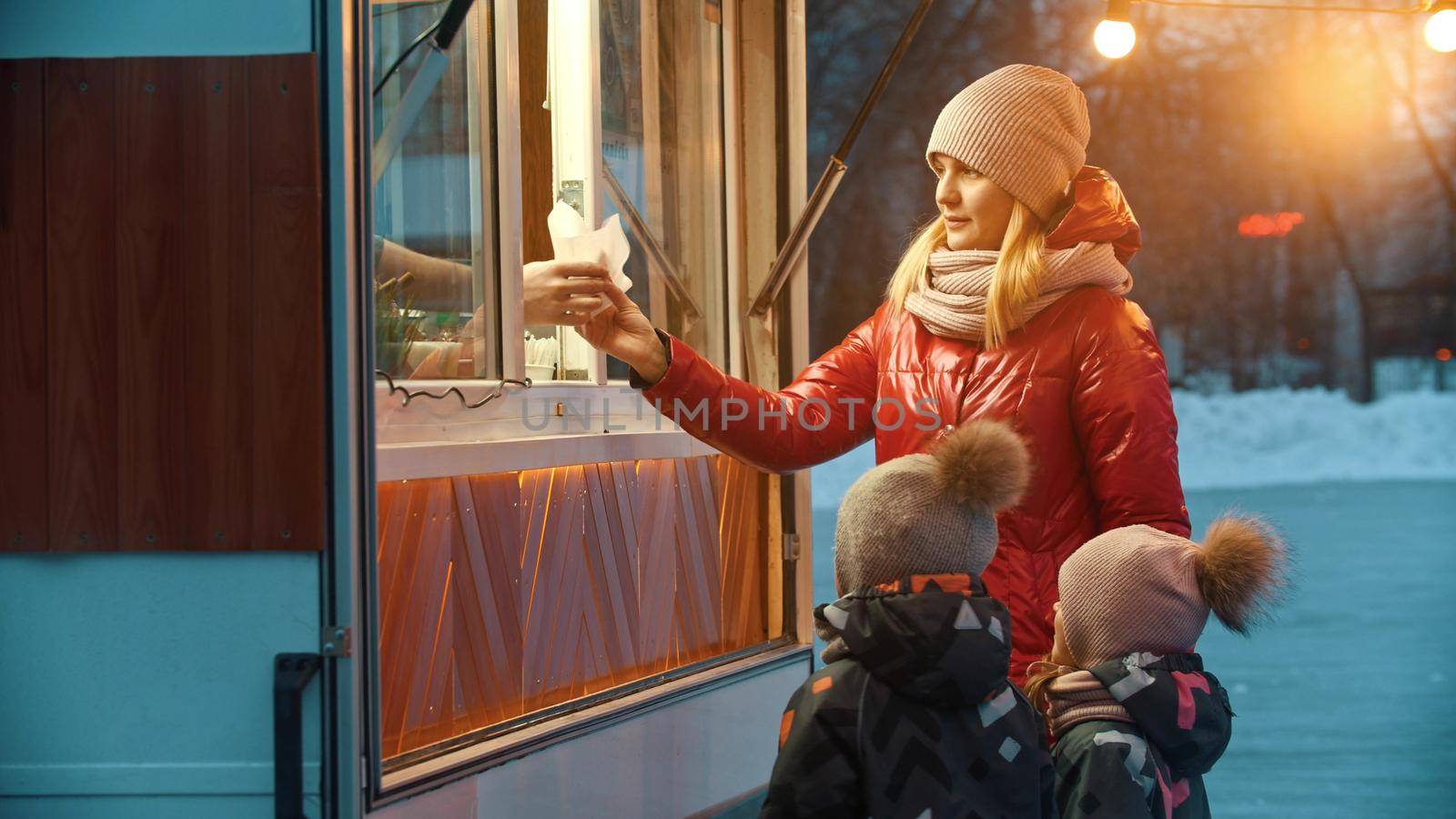 A young woman mother with her children standing near a little bright shop near the ice rink by Studia72