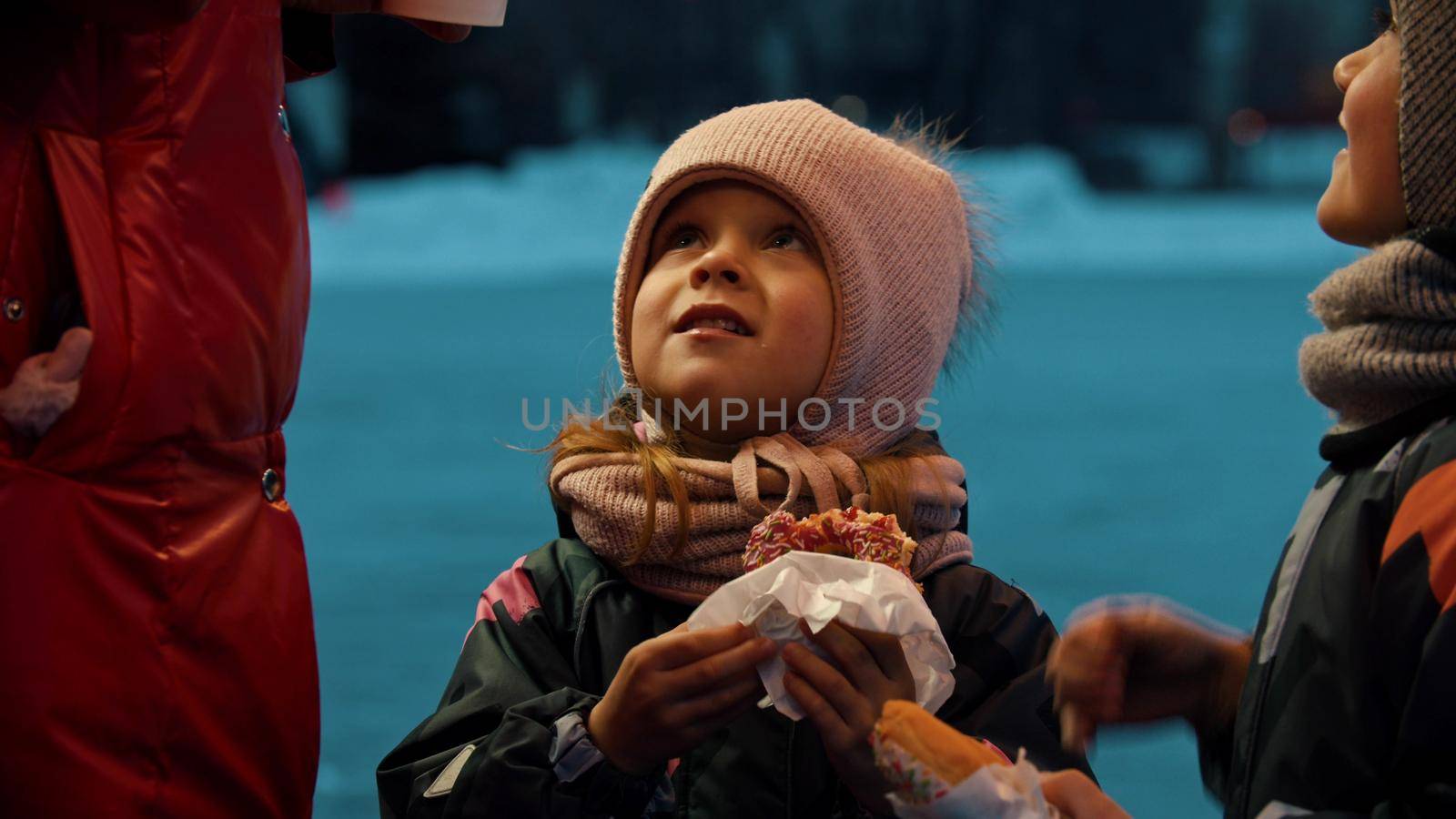 A little girl and boy eating donuts outdoors - the girl looking at her mother. Mid shot