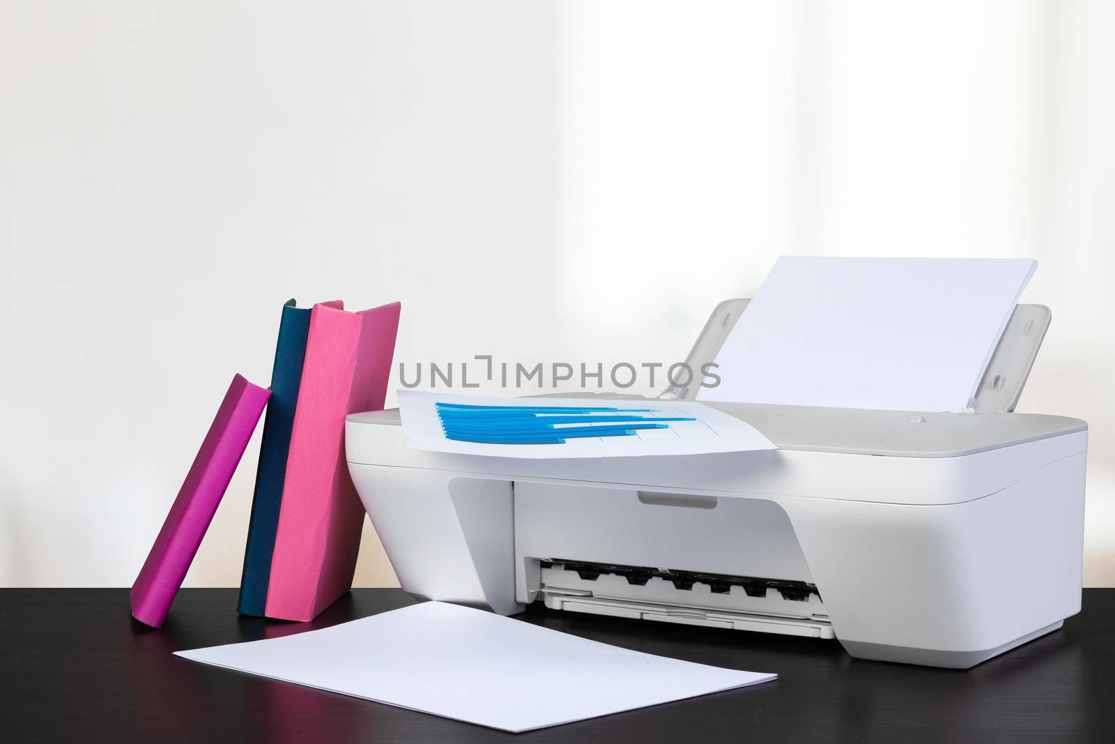 Compact home printer on desk with books against blurred background, close up