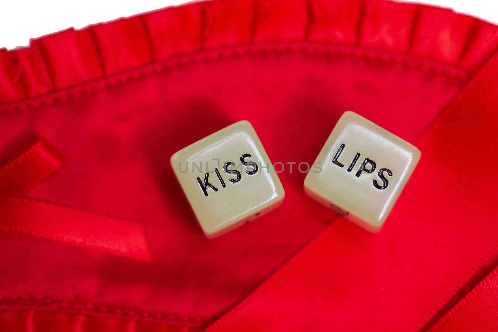 Two erotic dice for sexual game couple relation on red satin background texture isolated on white background top view with the text Kiss navel or lips Valentines Day, sex, romantic, sensual concept