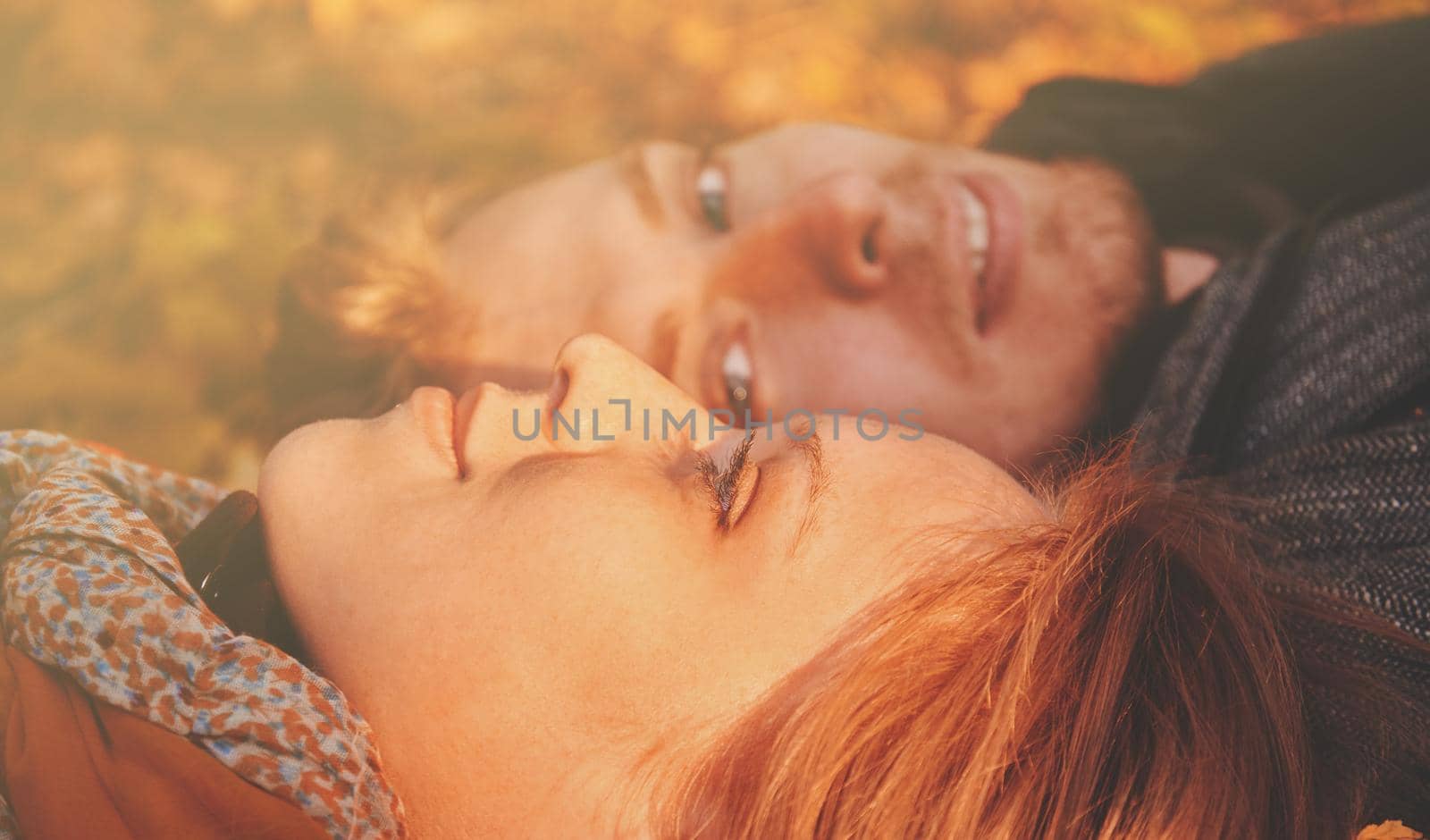 Loving couple lying on autumn leaves in the park. Image with sunlight effect.