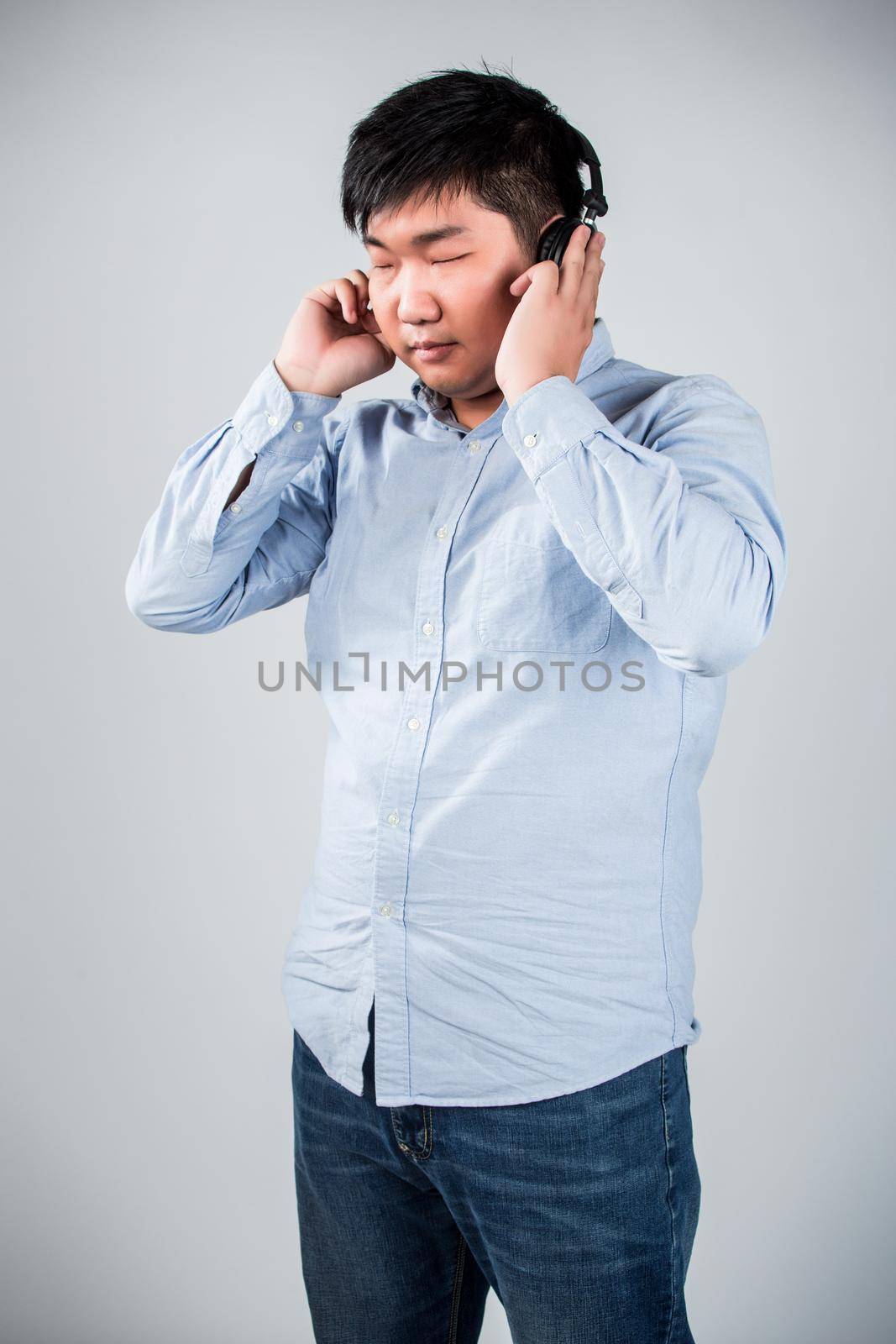 Love this music. Handsome young man in headphones holding mobile phone and smiling while standing against grey background