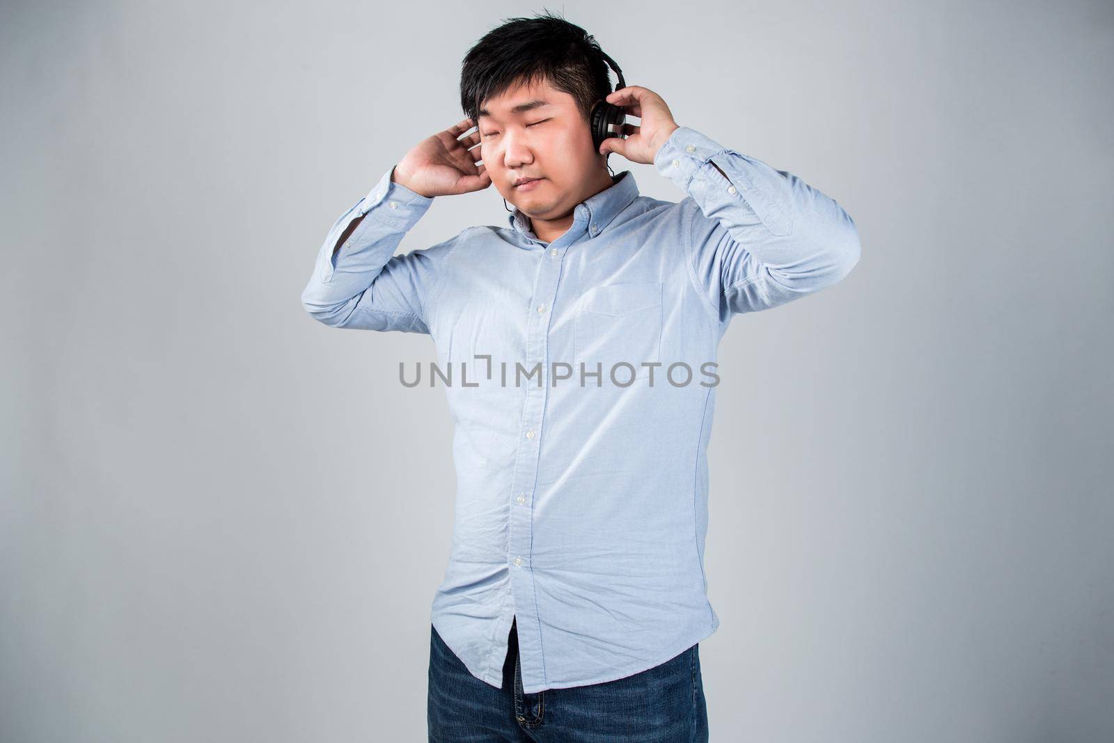 Love this music. Handsome young man in headphones holding mobile phone and smiling while standing against grey background