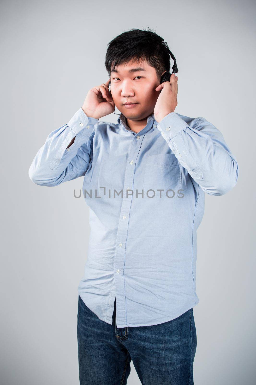 Love this music. Handsome young man in headphones holding mobile phone and smiling while standing against grey background