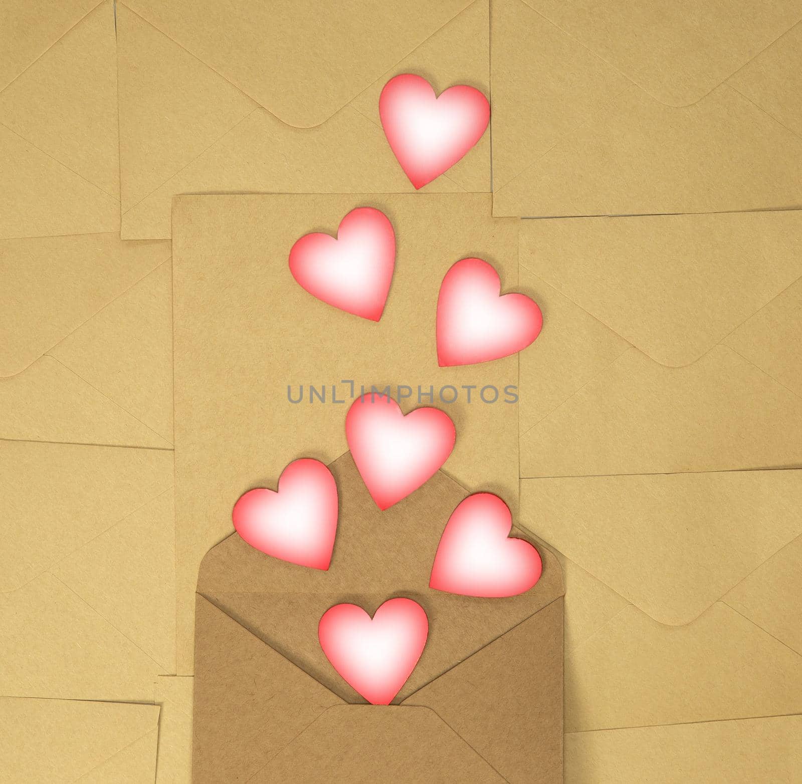 Paper craft envelope with pink hearts on brown plain background. Concept of love and Valentines Day, top view copy space. Romantic design