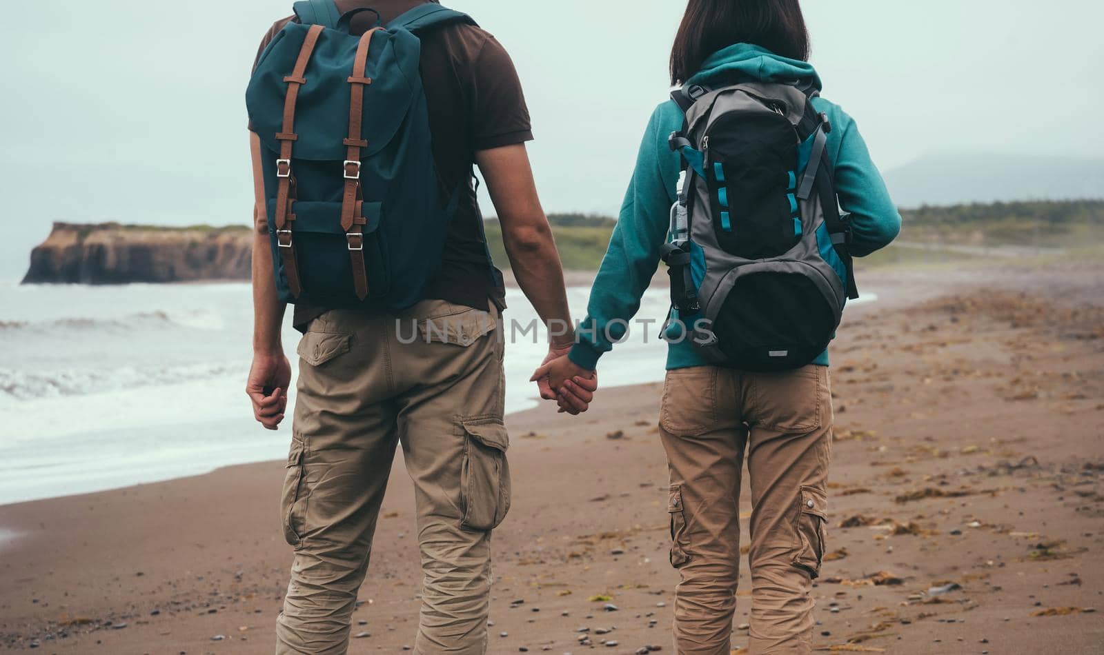 Traveler couple in love with backpacks walking on sea beach in summer and holding each other hand