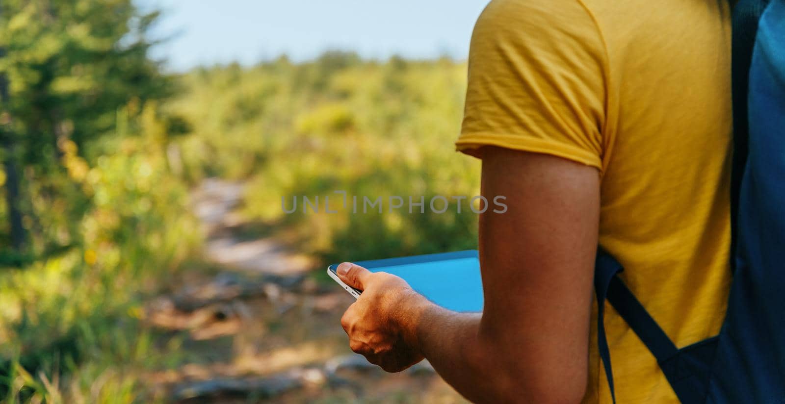 Unrecognizable hiker man searches GPS coordinates on tablet PC in summer forest