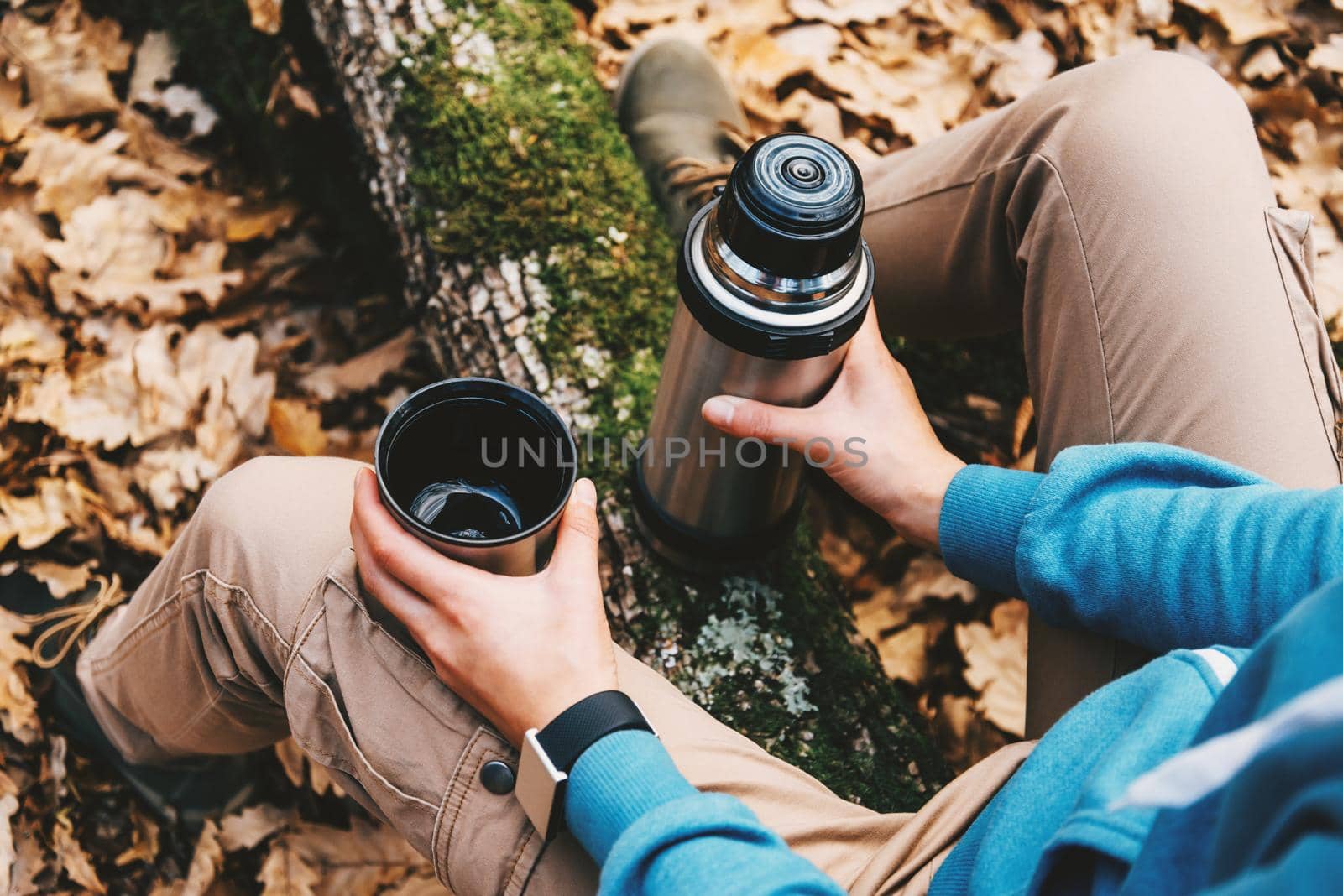 Unrecognizable traveler woman holding a cup of tea or coffee and thermos in autumn forest. Hiking and leisure theme