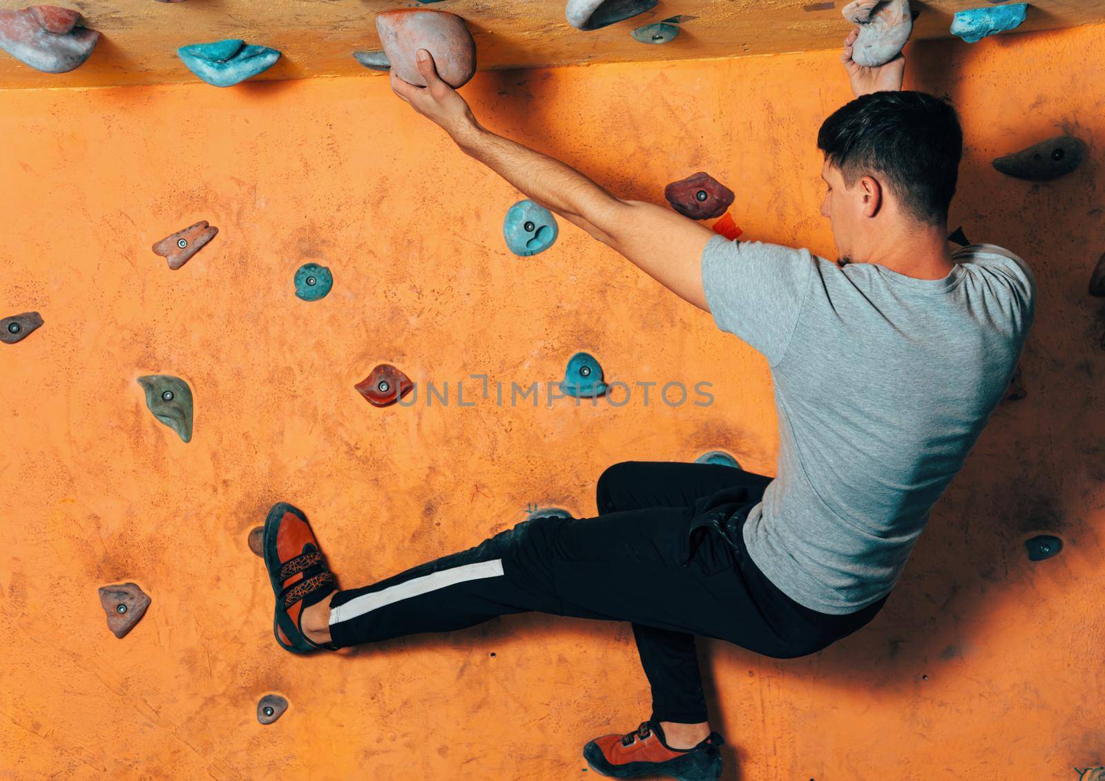 Young man climbing up on wall in gym, side view