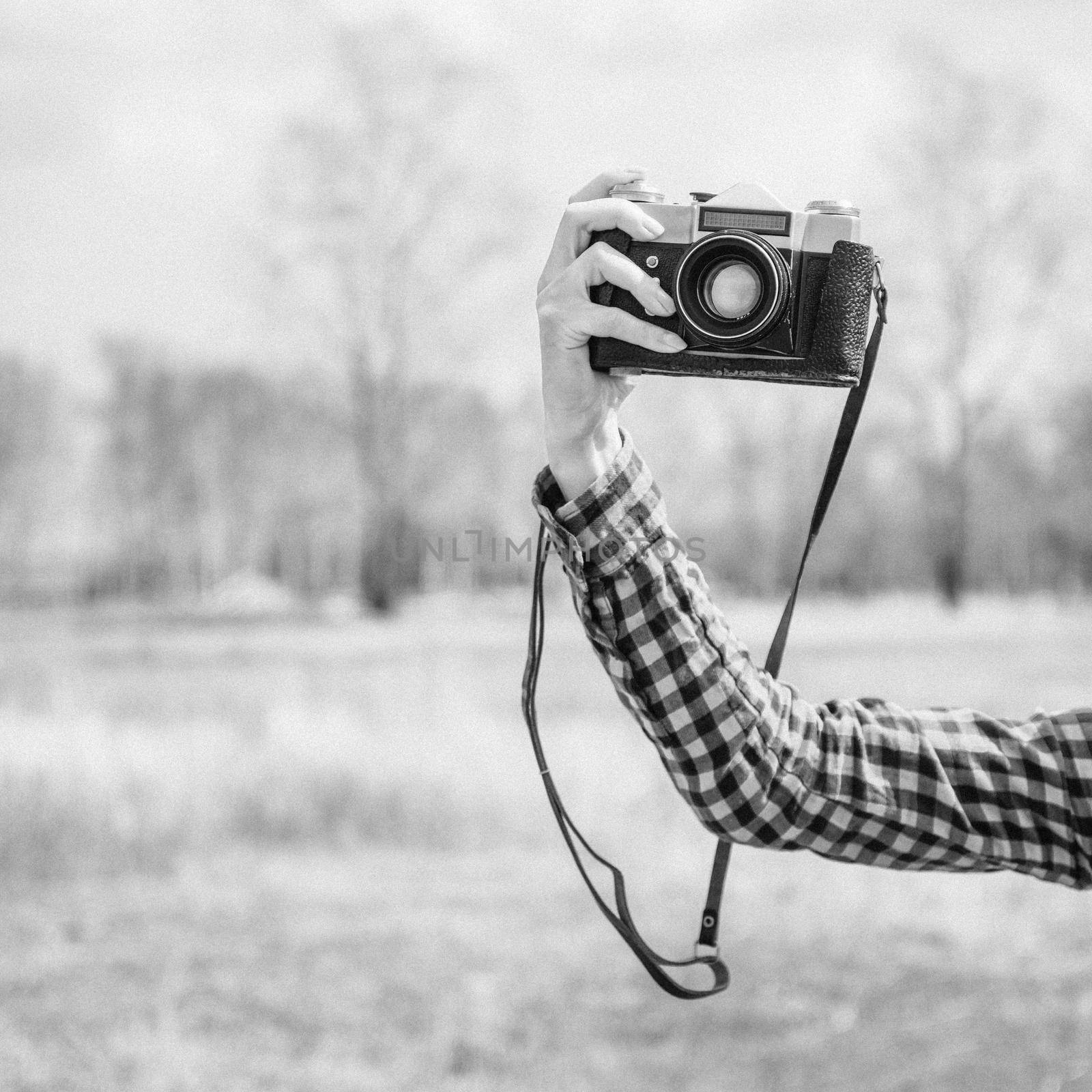 Female hand with vintage photo camera outdoor. With film grain and low contrast effect. Black-white photo.