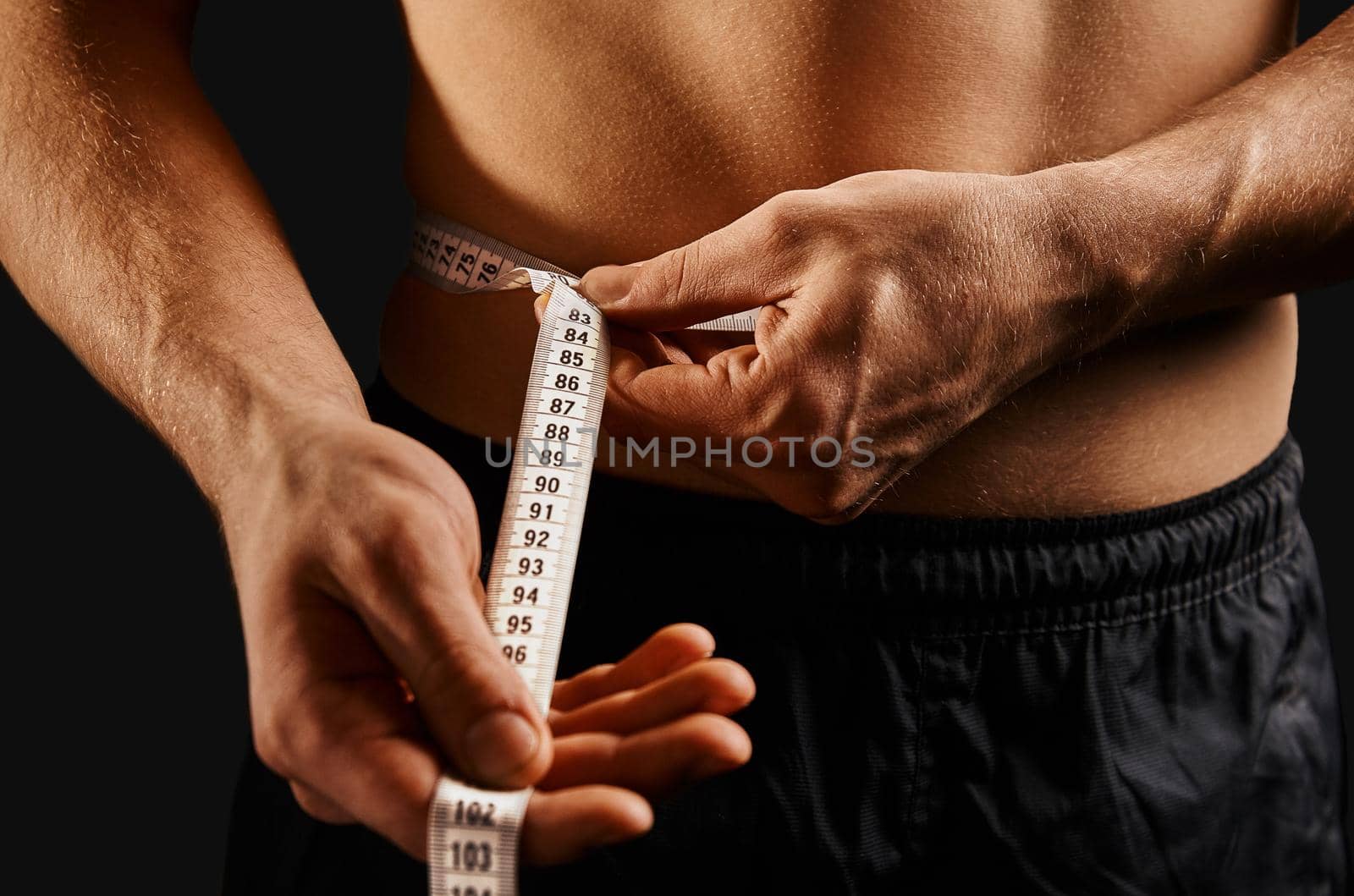 Unrecognizable sportsman measuring waist with centimeter tape