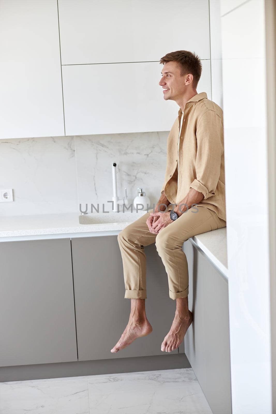 Happy handsome man is standing on minimalistic kitchen and smiling