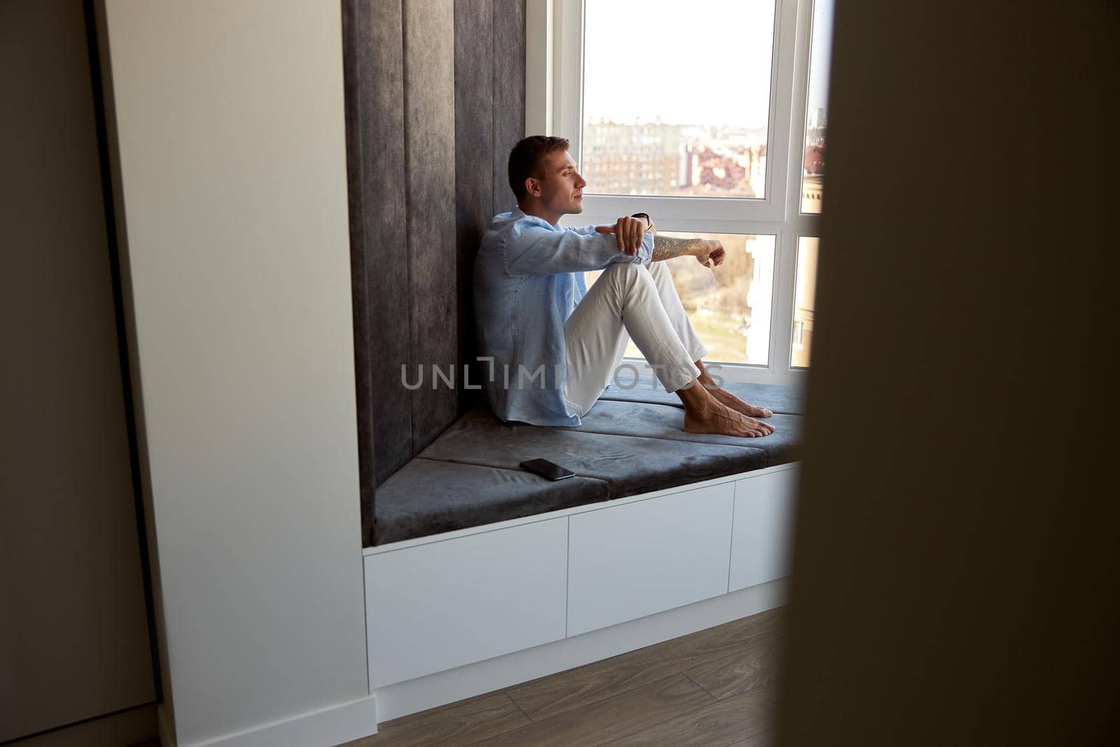 Happy adult caucasian male is sitting near panoramic window and chilling by Yaroslav_astakhov