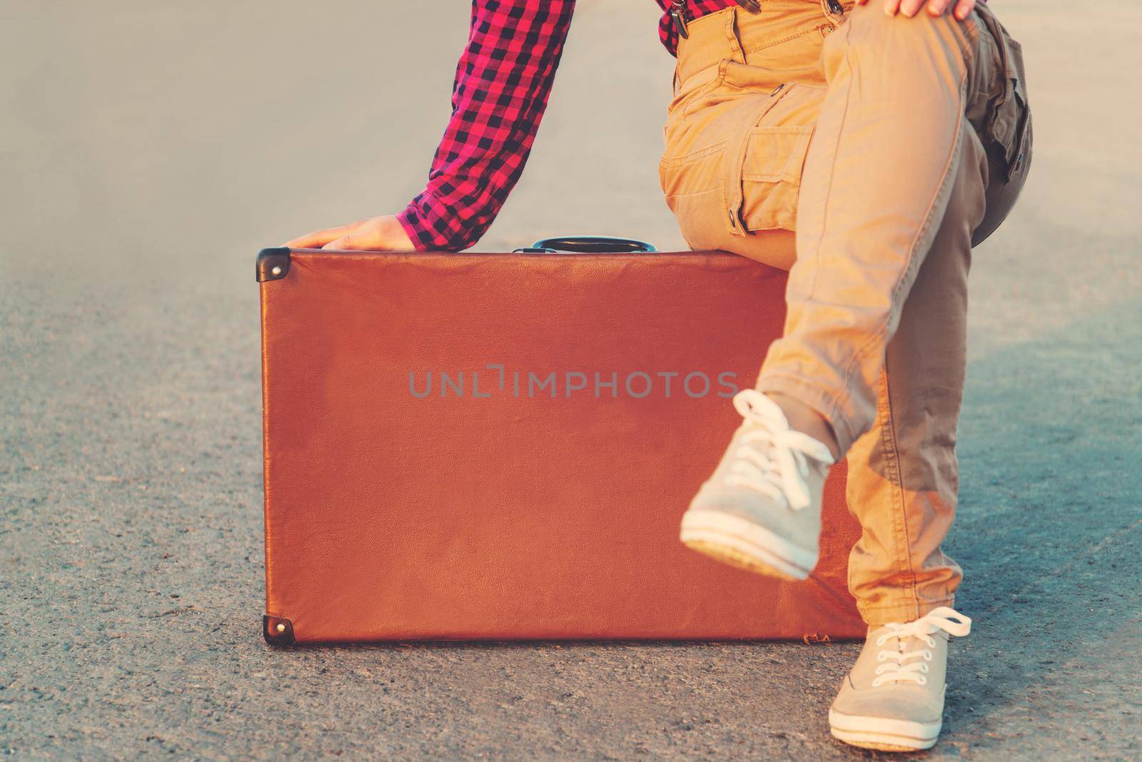 Unrecognizable woman traveler sitting on suitcase