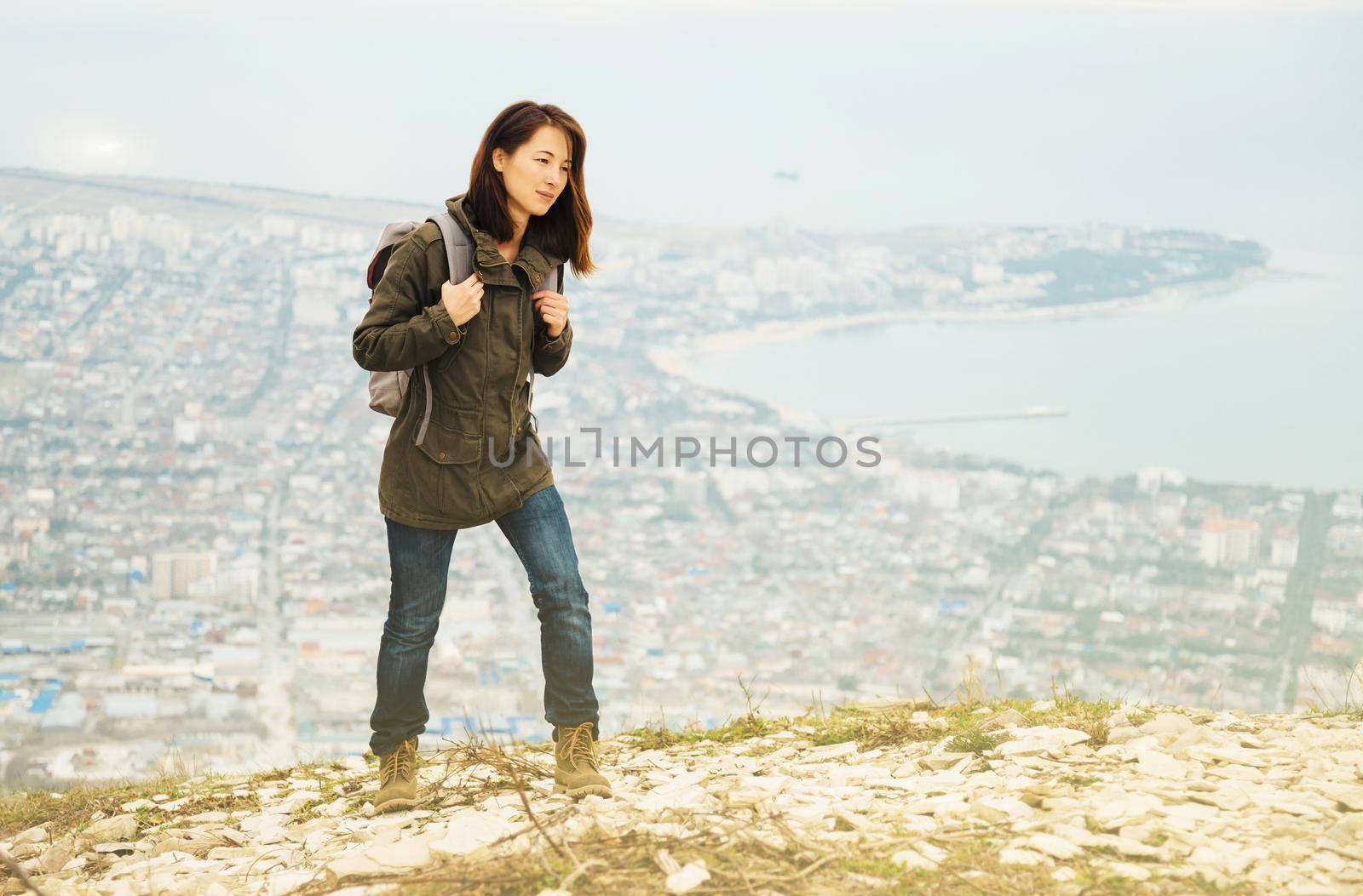 Young traveler woman with backpack walking in highlands over the city. Hiking and recreation theme