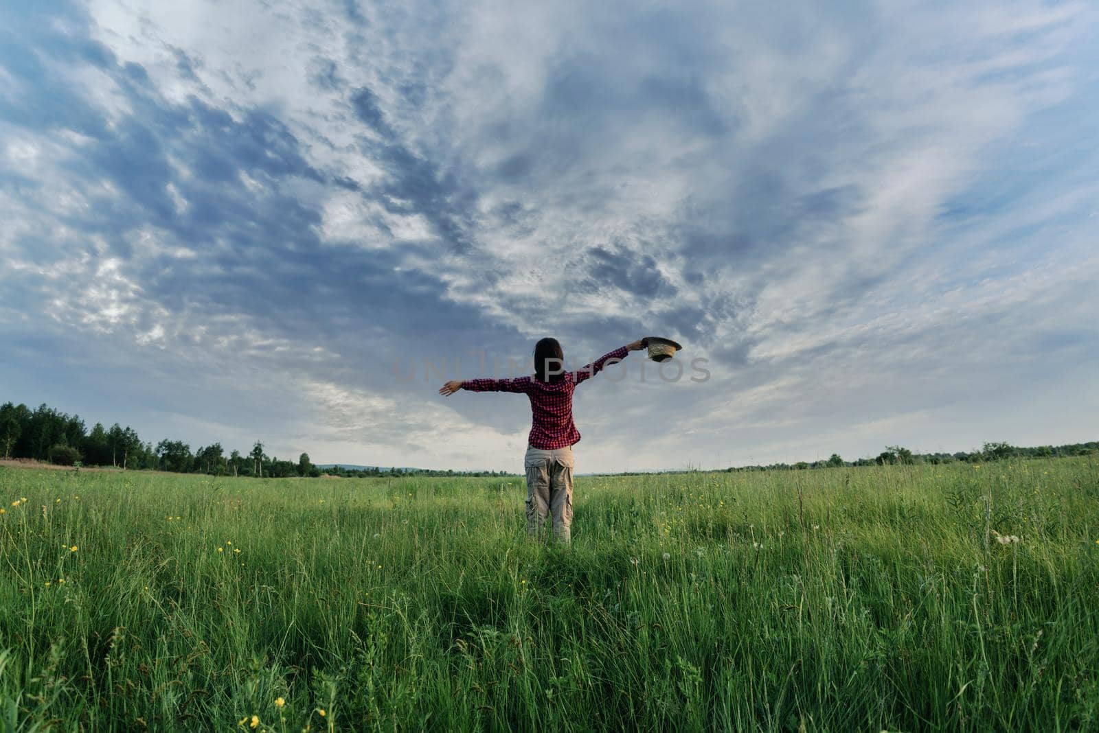Hipster girl with her arms wide spread is enjoying a sunny summer day, rear view