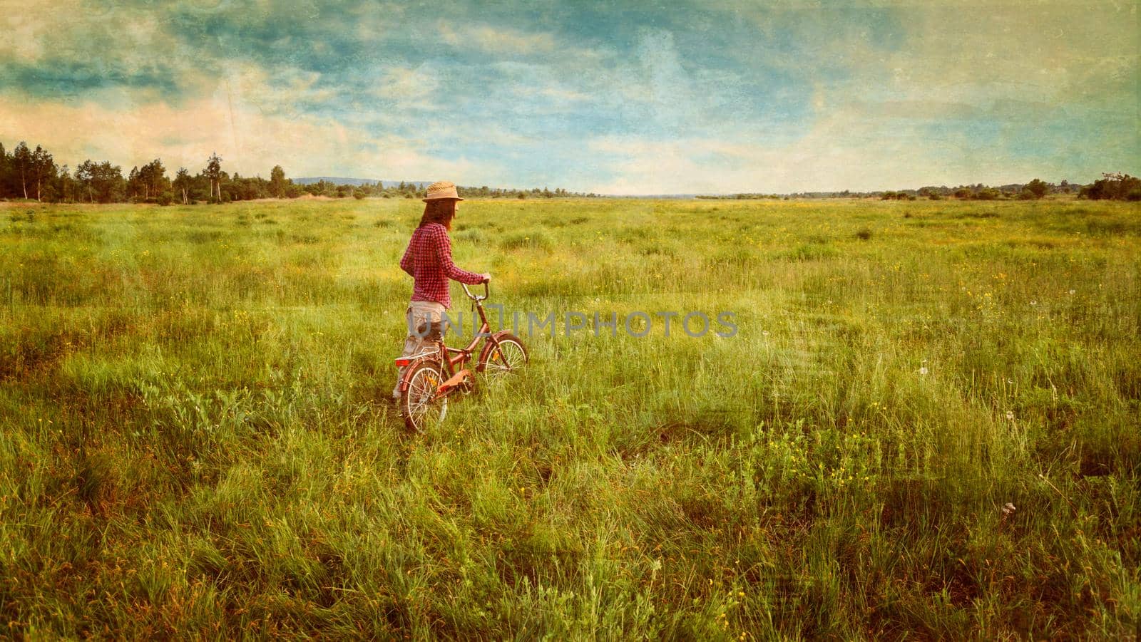 Hipster girl in straw hat walking with bicycle on summer meadow outdoor. Vintage image