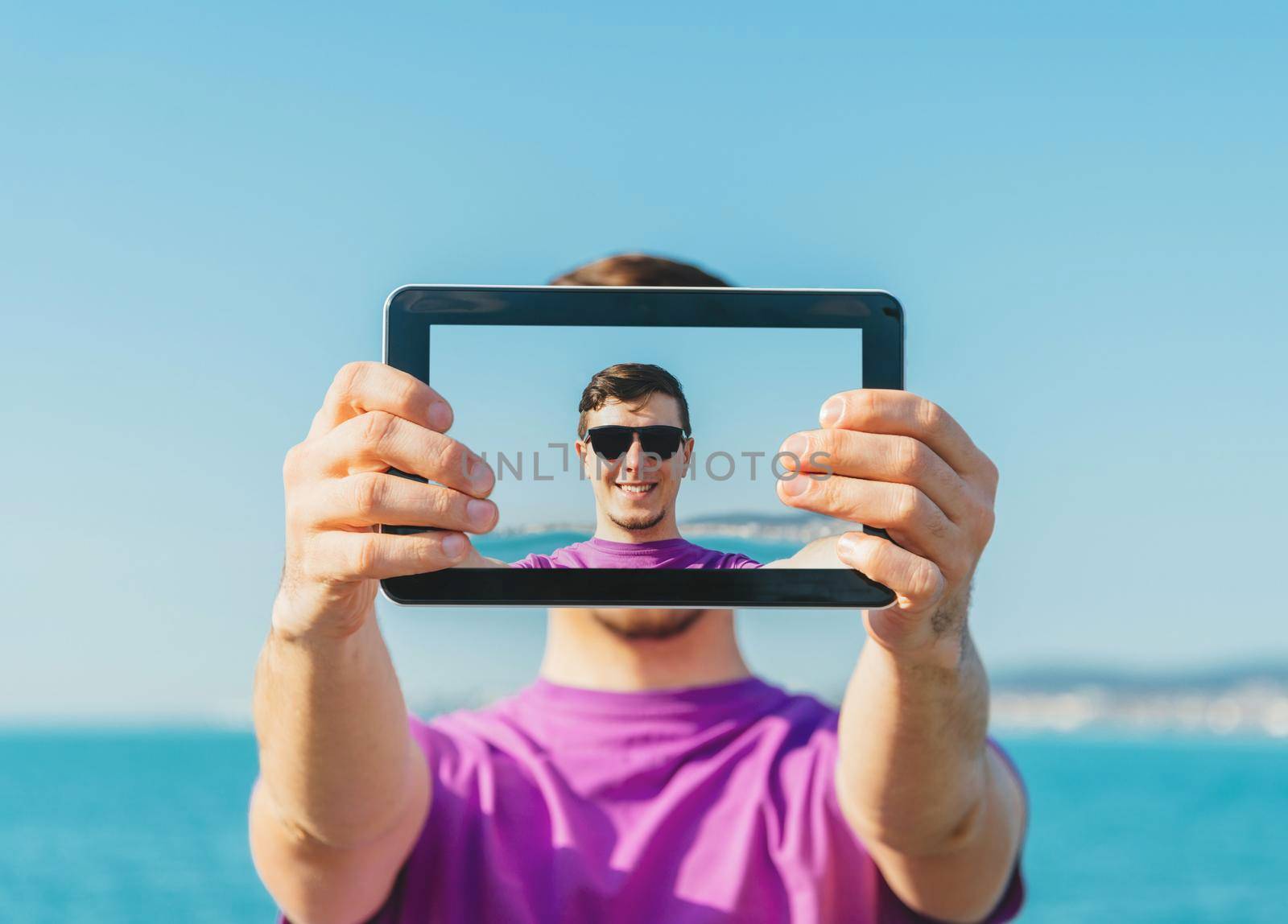 Young smiling handsome man doing a self-portrait with him digital tablet on background of sea