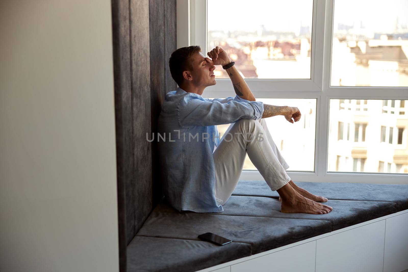 Happy adult caucasian male is sitting near panoramic window and chilling by Yaroslav_astakhov